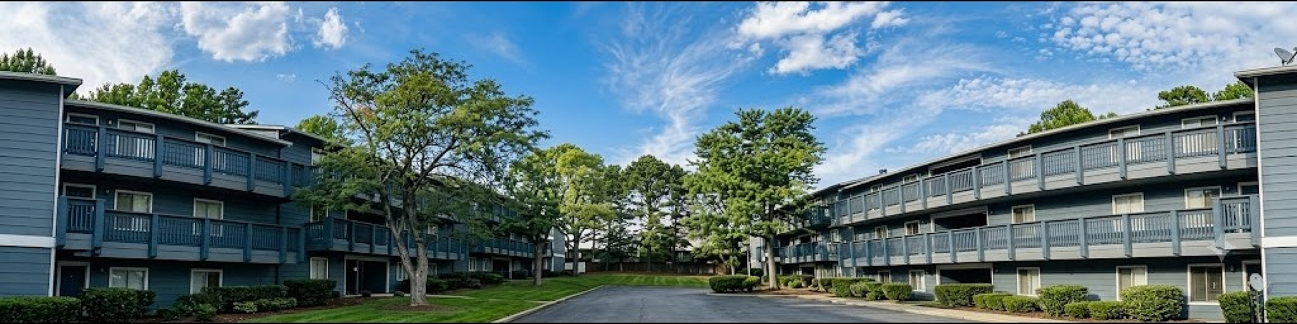 Charming apartment complex nestled among lush greenery with modern architecture and inviting balconies against a bright blue sky.