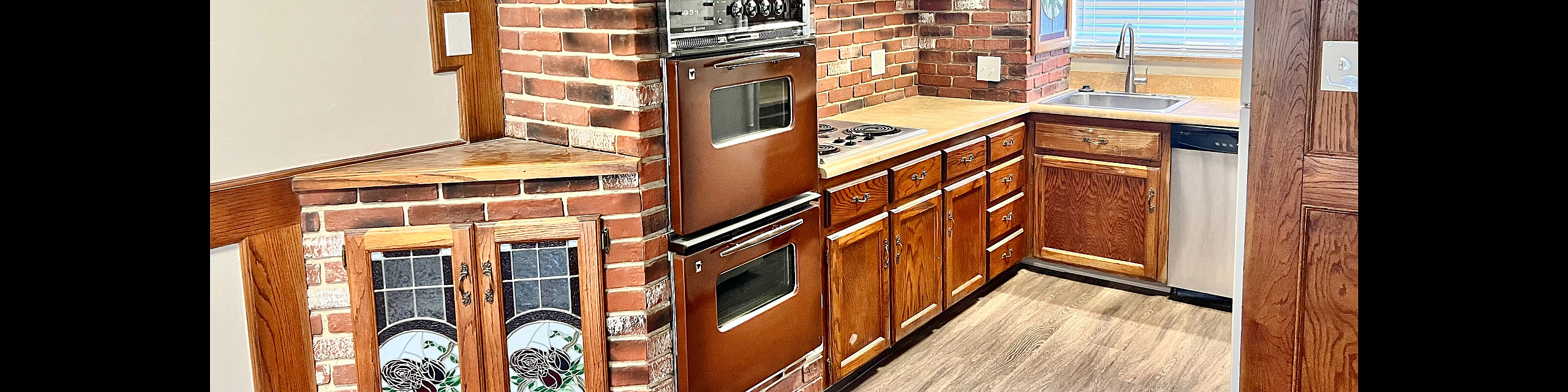 Charming kitchen with rustic brick accents, elegant stained glass cabinets, and modern appliances offering a cozy and inviting atmosphere.