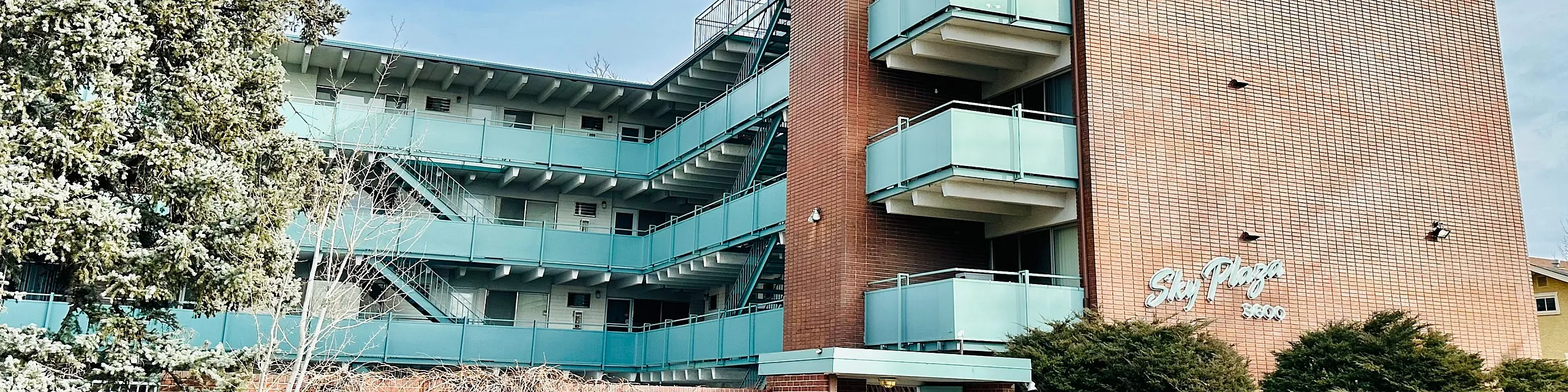 Charming mid-century modern apartment building with vibrant turquoise balconies and lush greenery in a serene neighborhood.
