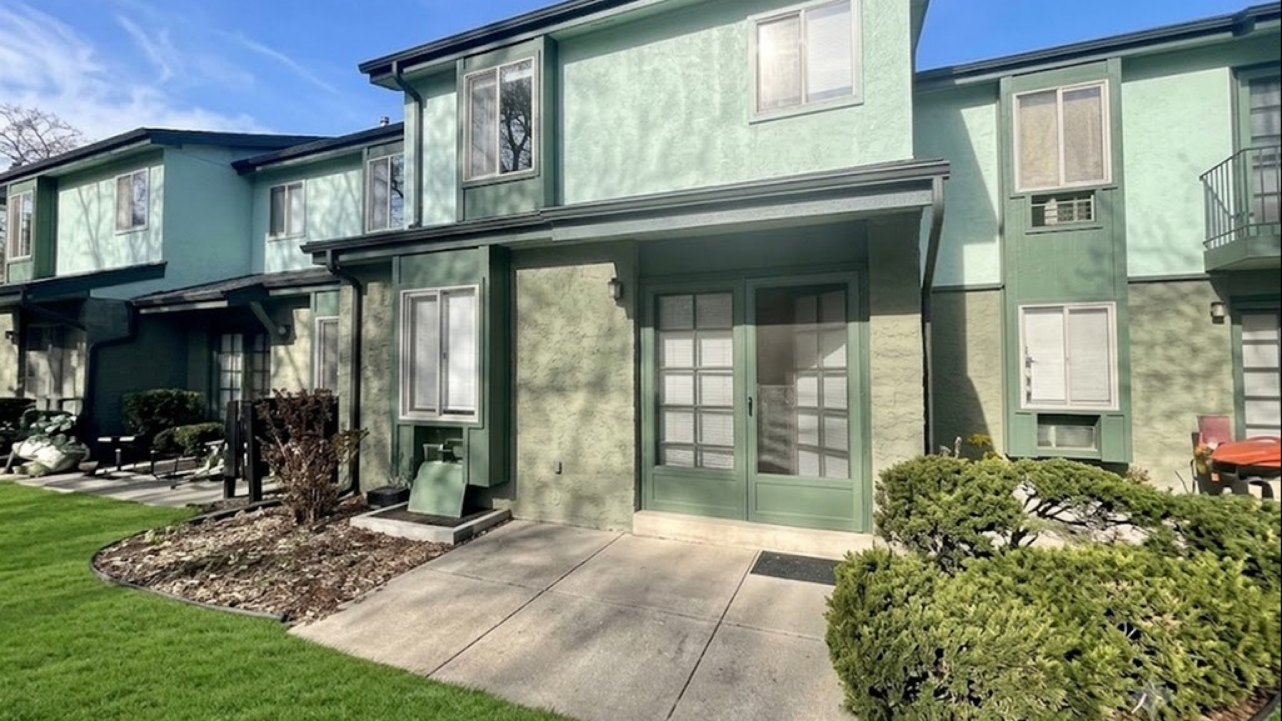 Charming townhouse exterior with lush green lawn and sun-drenched patio, perfect for vibrant outdoor living.