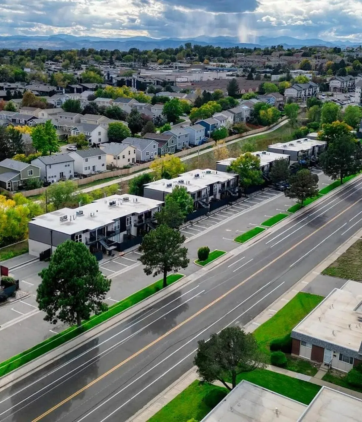 Breathtaking aerial view of a vibrant suburban neighborhood with lush greenery, modern architecture, and scenic mountain backdrop.