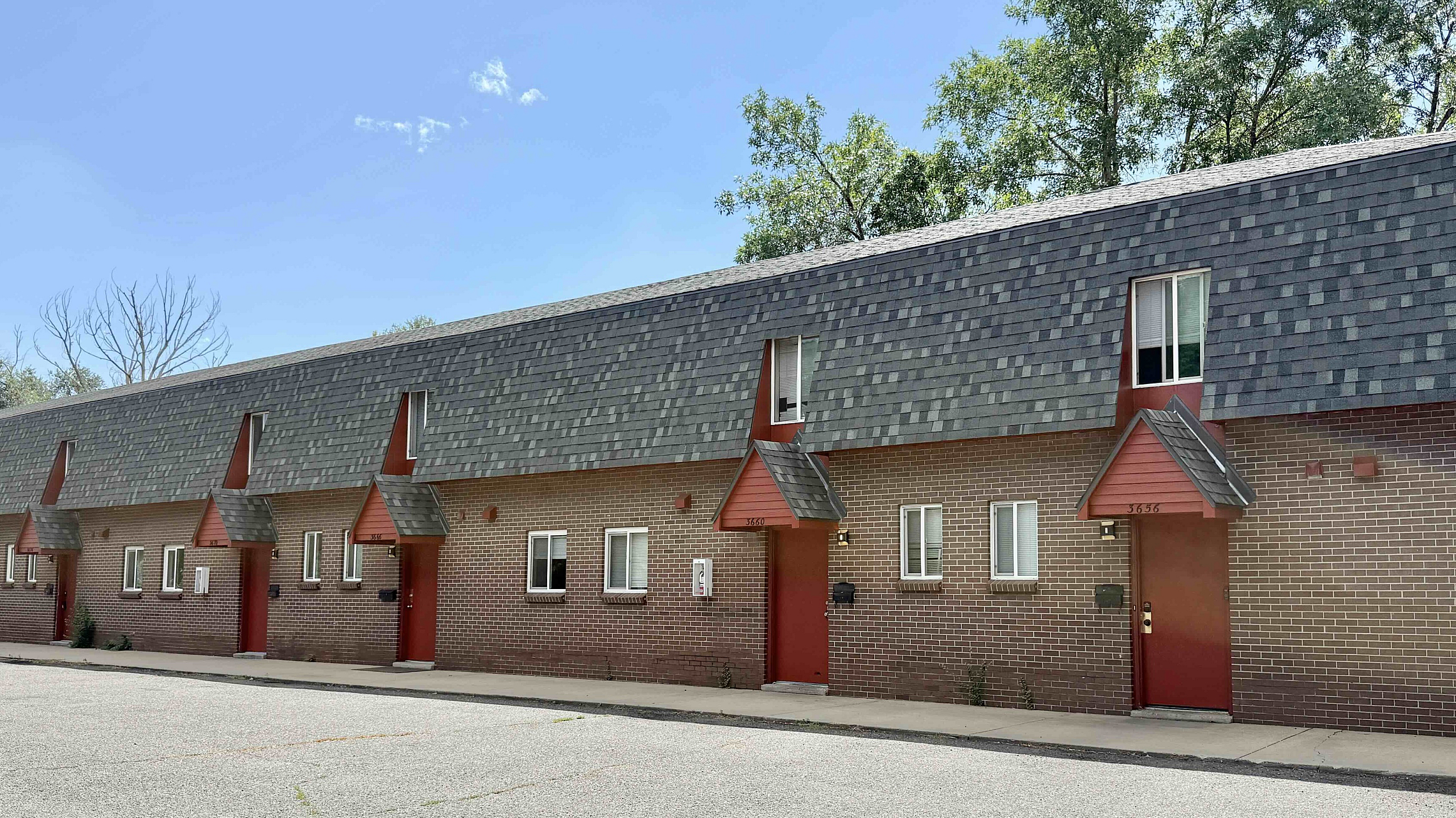 Charming brick apartment complex with distinctive peaked roofs, offering a serene residential atmosphere surrounded by lush greenery.