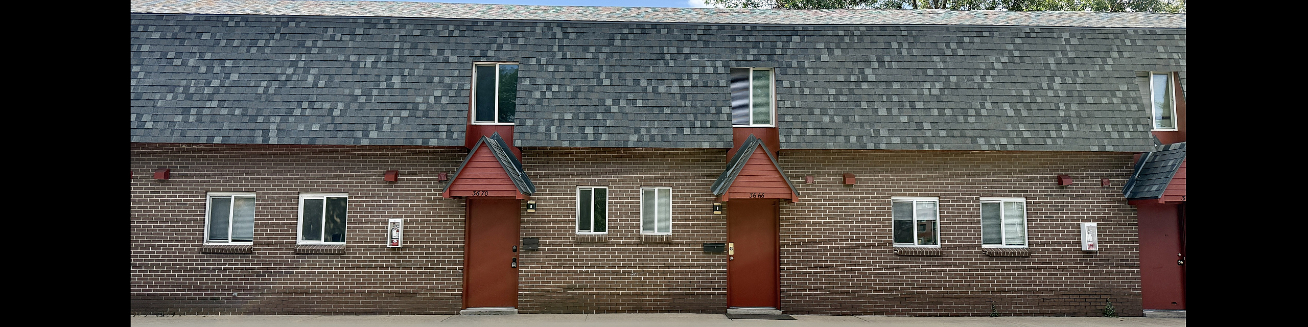 Charming townhouse with brick exterior, modern roofing, and inviting red accents, nestled in a serene neighborhood.