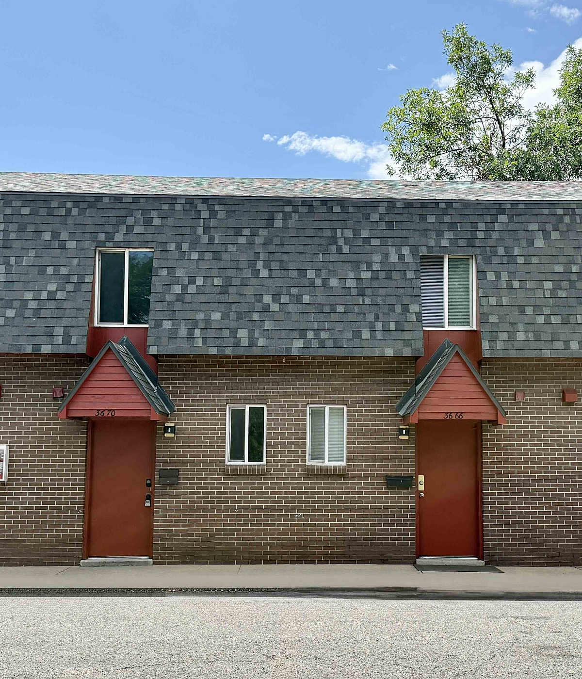 Charming townhouse exterior with brick facade, red doors, and modern shingles, perfect for cozy living.