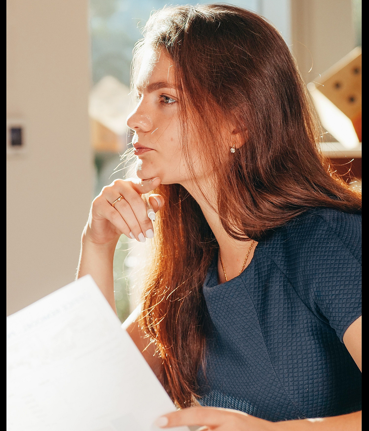 Thoughtful person reviewing documents by a sunlit window, creating a serene and productive atmosphere.