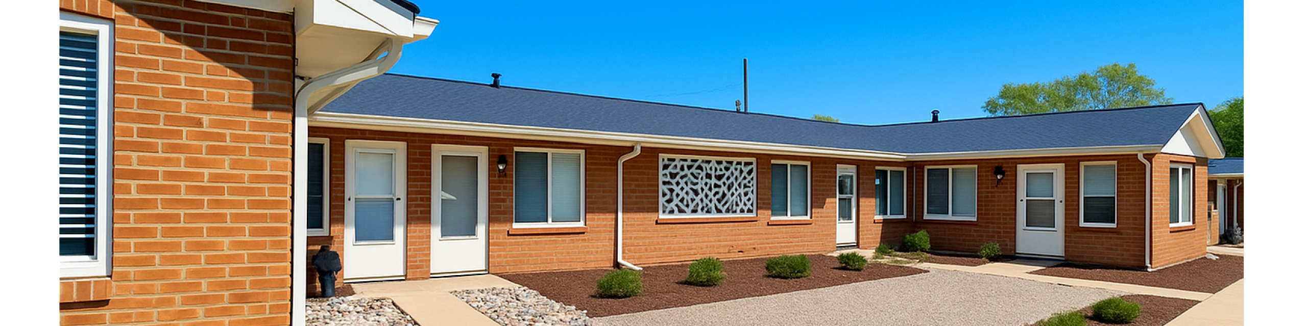 Charming brick apartment complex with modern design, featuring well-maintained pathways and lush landscaping under a clear blue sky.