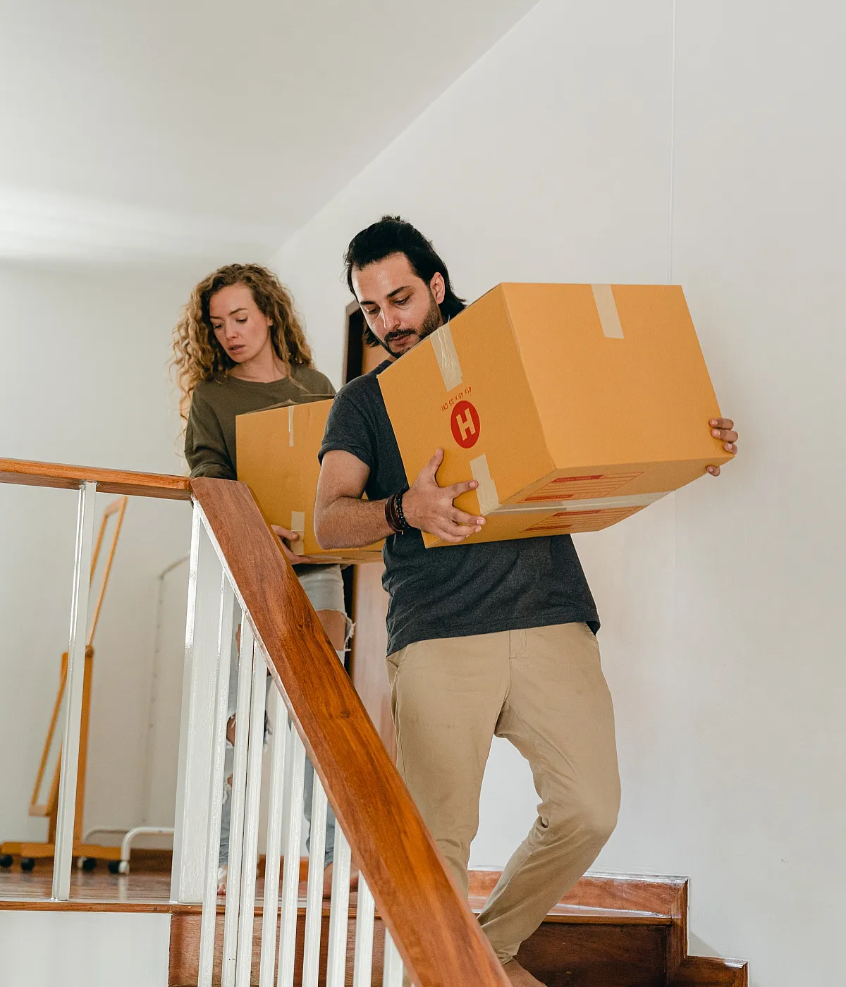 Couple moving boxes down a modern wooden staircase, showcasing a bright and welcoming interior perfect for new beginnings.