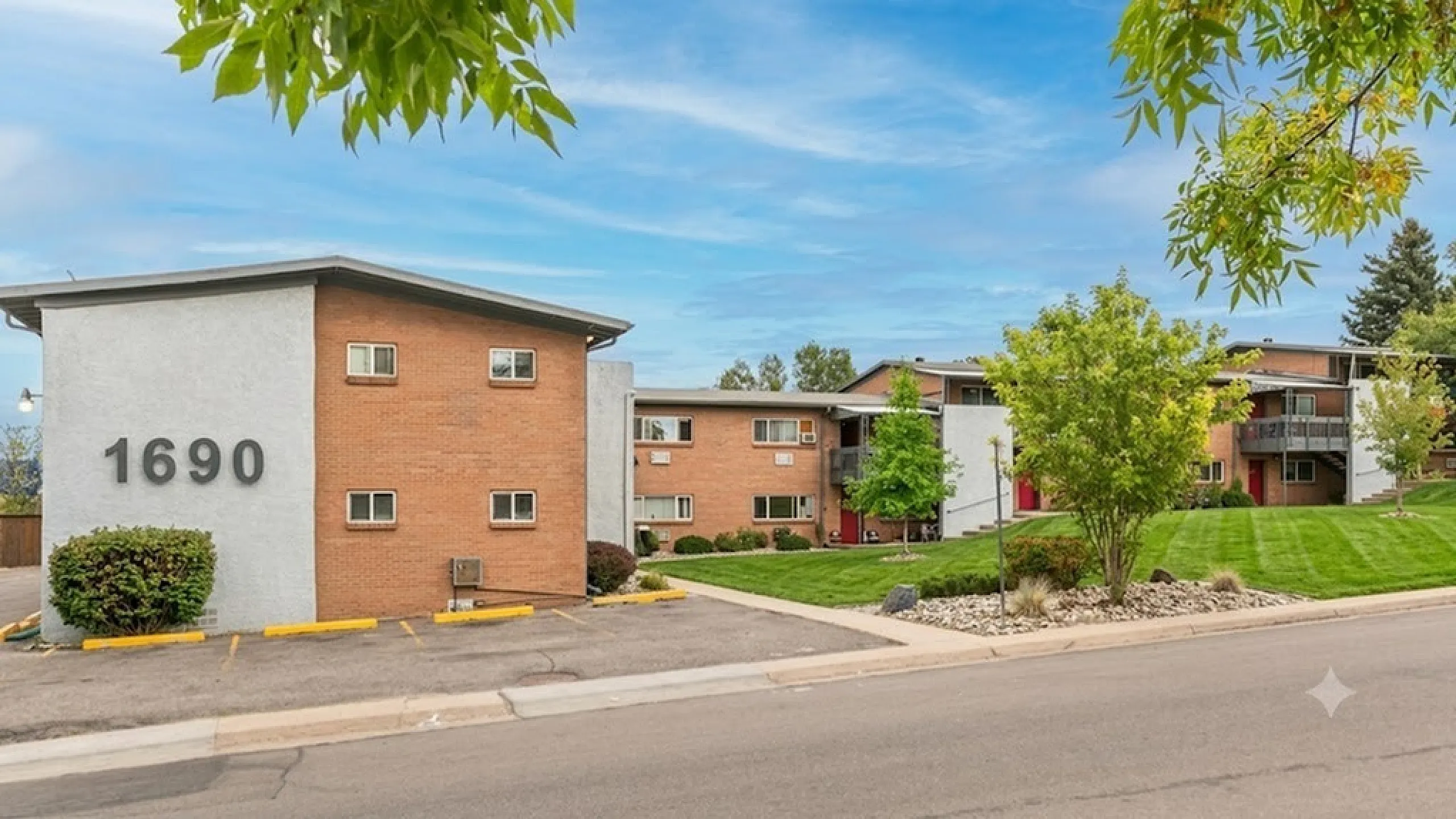 Charming apartment complex with a modern brick facade, nestled in a lush green landscape under a bright blue sky.