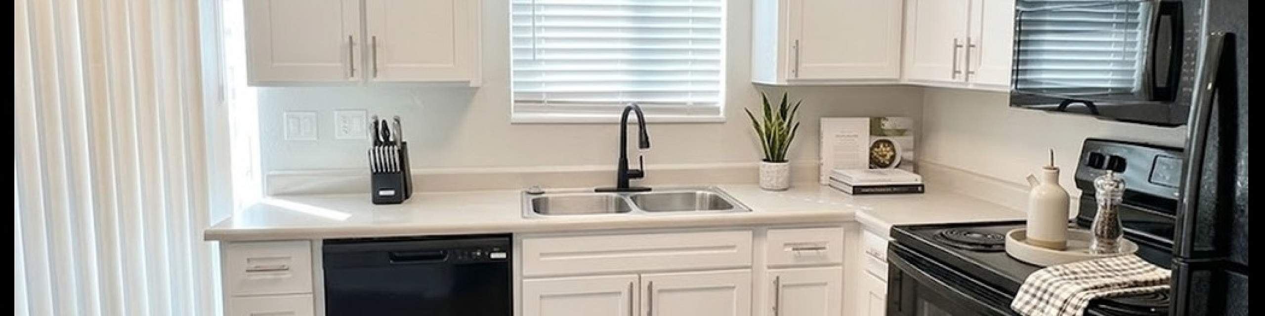 Bright, modern kitchen with sleek black appliances, white cabinetry, and elegant wood flooring.