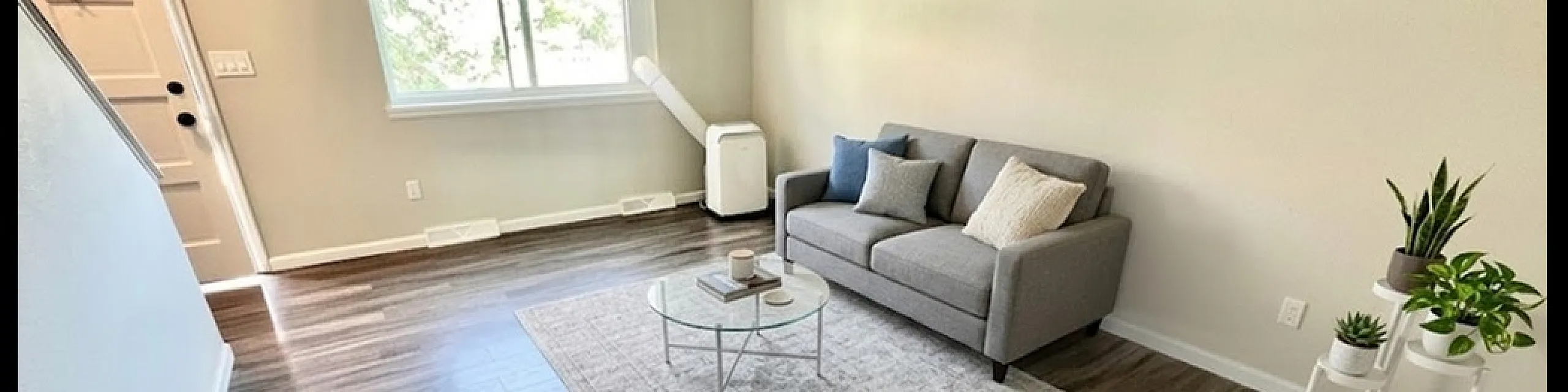 Bright and inviting living room with modern decor, featuring sleek wood flooring, a comfortable gray sofa, elegant coffee table, and abundant natural light from a large window.