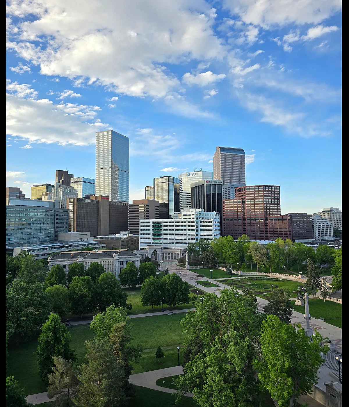 Vibrant cityscape view featuring modern skyscrapers and lush green park, under a serene blue sky.