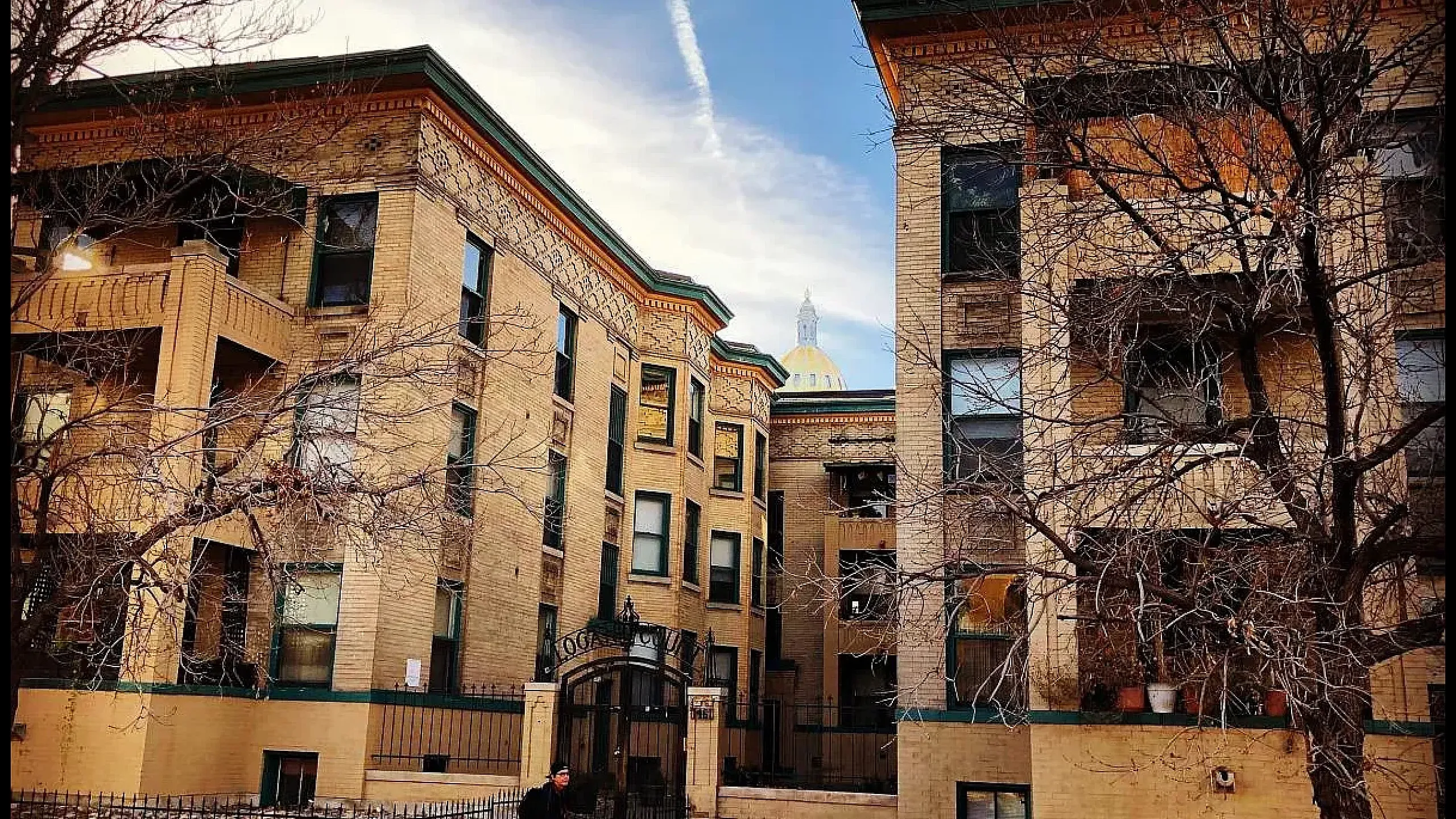Charming courtyard view of modern brick apartment buildings, featuring lush green lawns and a vibrant communal space under a picturesque sky.