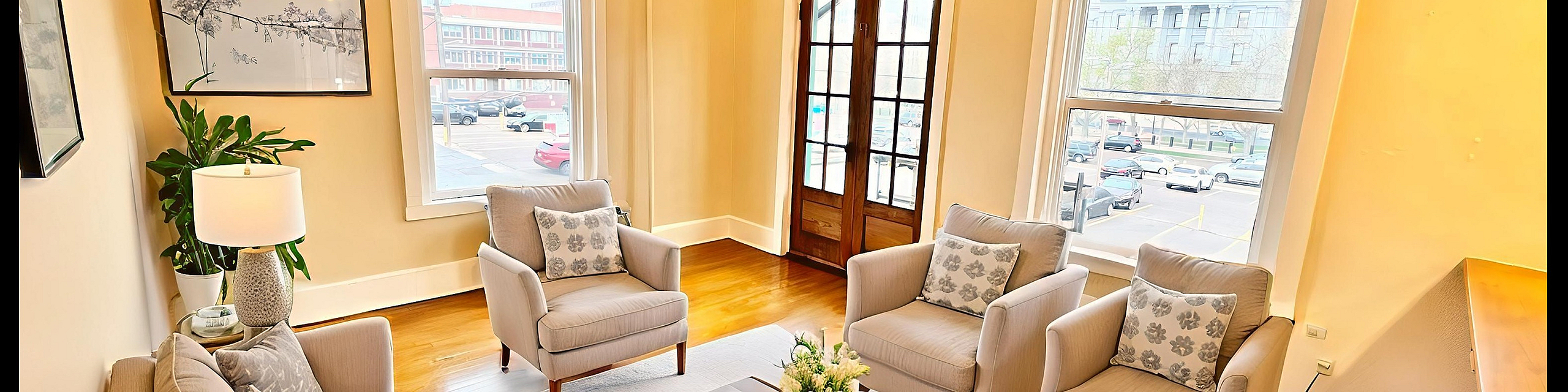 Bright, inviting living room with elegant beige seating, natural light through large windows, and charming hardwood floors.