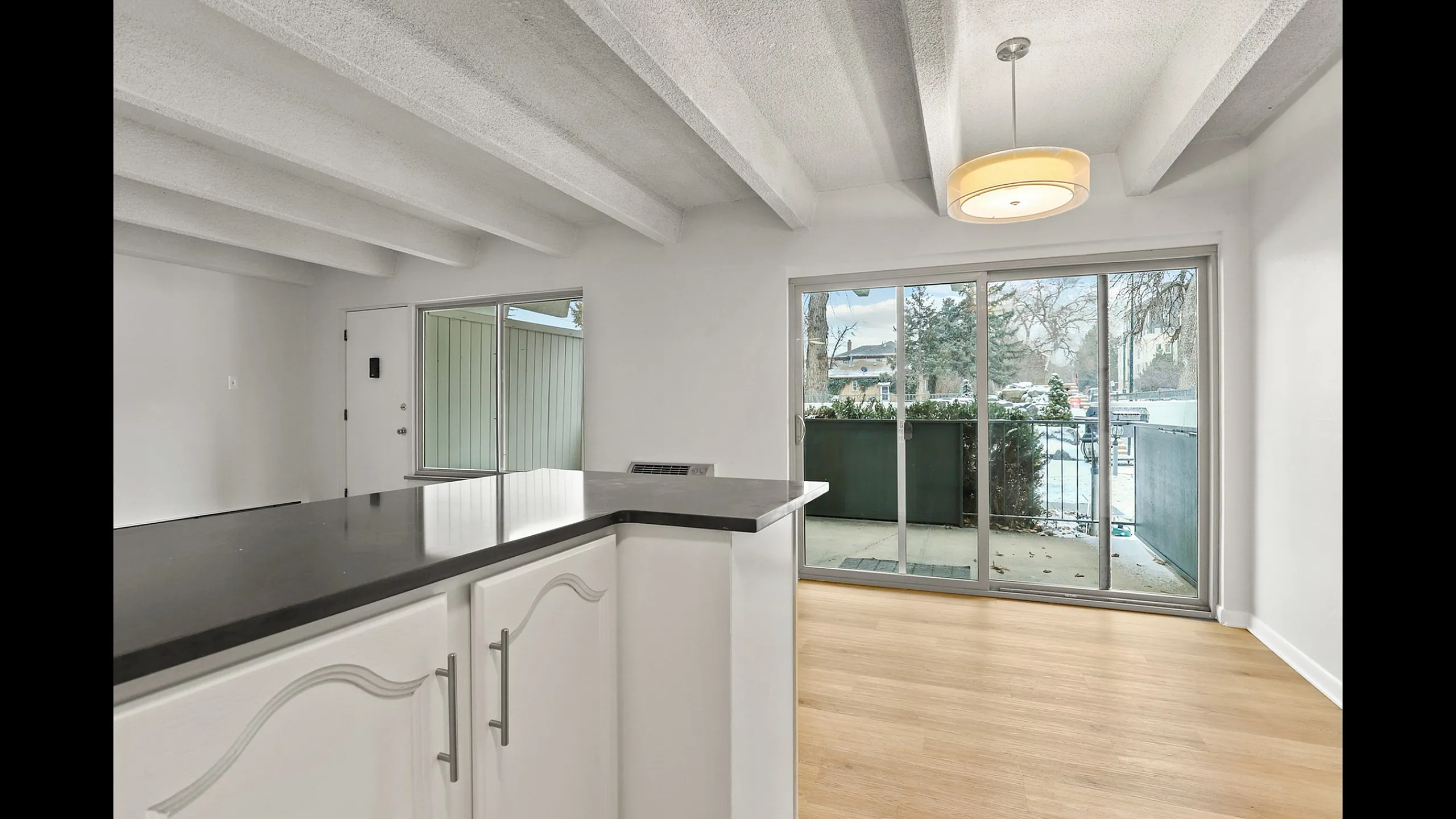 Bright open-concept apartment featuring a modern kitchen with sleek countertops, large windows, and a cozy outdoor balcony view.