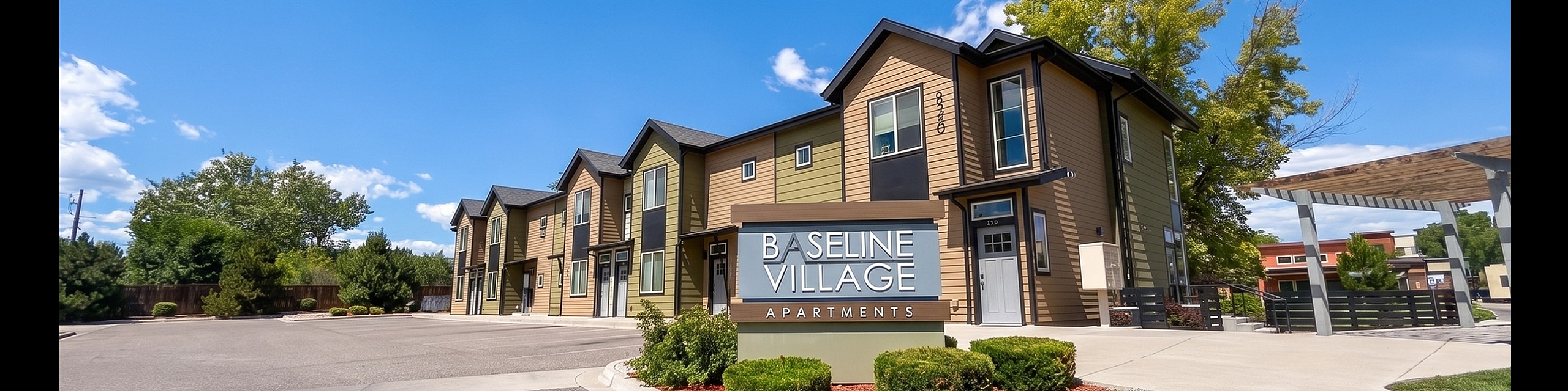 Charming Baseline Village Apartments with contemporary architecture and lush landscaping under a vibrant blue sky.