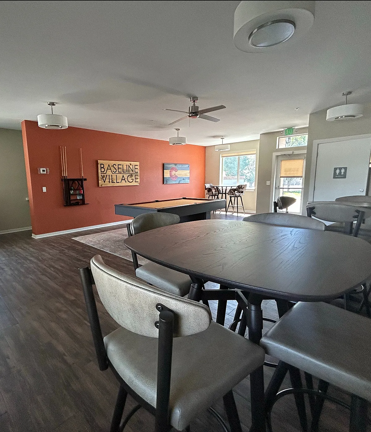 Inviting community room in Baseline Village with sleek wooden flooring, ample seating, and entertainment amenities including a pool and foosball table.