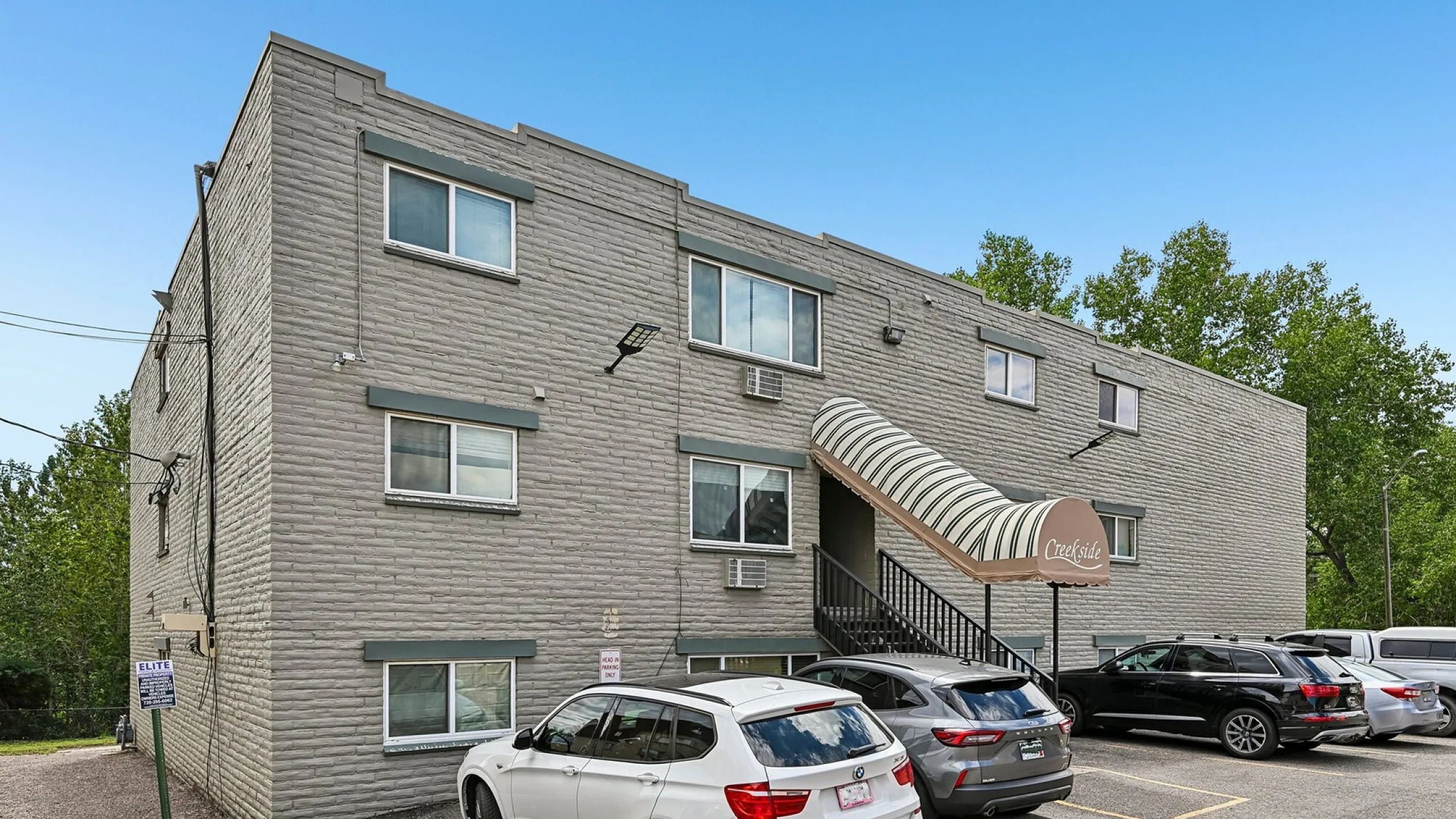 Inviting apartment building with contemporary brick facade and ample parking, nestled in a serene, tree-lined area.