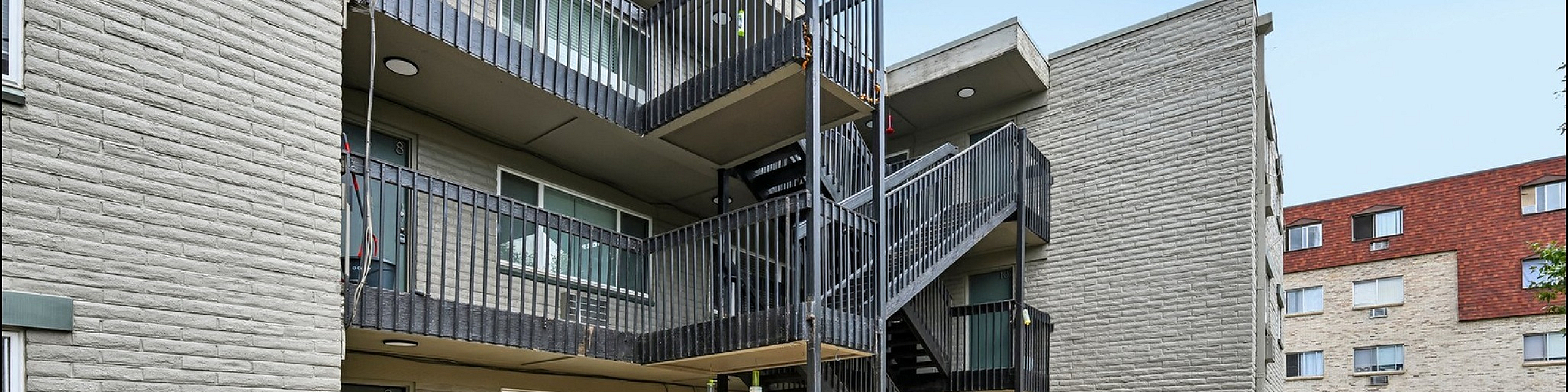 Inviting apartment exterior with modern brick design and accessible balconies, featuring a communal outdoor seating area and green accents.