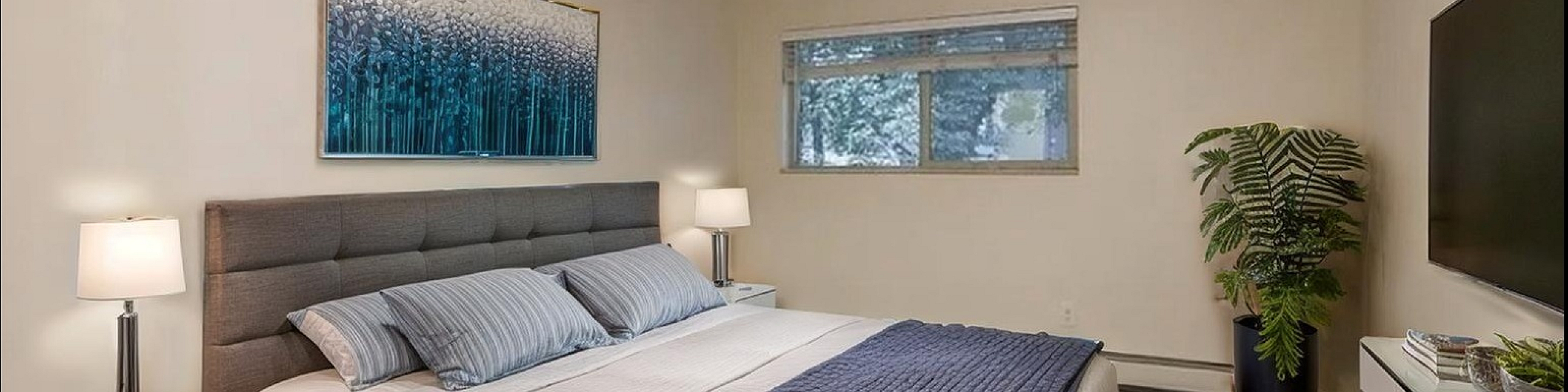 Inviting bedroom with modern decor, featuring a cozy bed, elegant nightstands, stylish ceiling fan, and a window with a view of lush greenery.