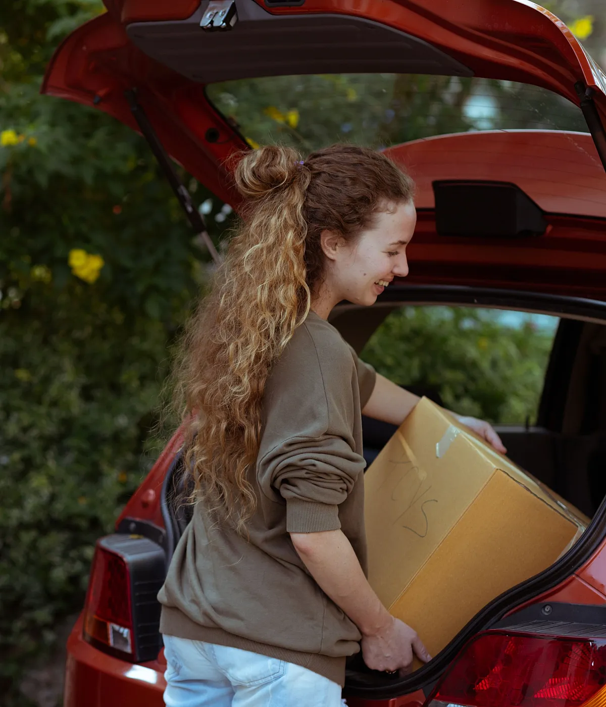 Joyful couple moving into their new home, unloading boxes from a car surrounded by lush greenery, signifying a fresh start and vibrant living.