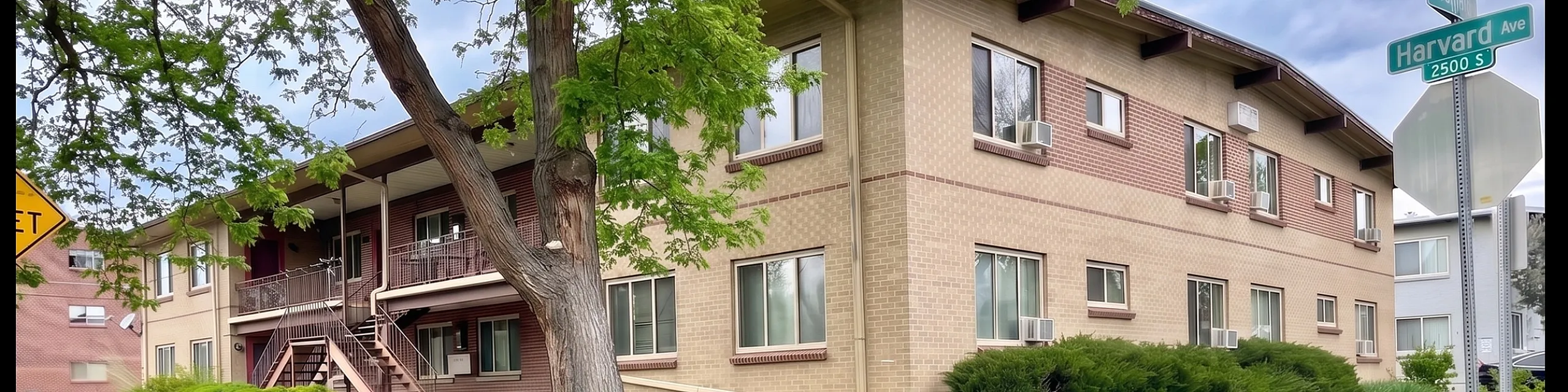 Charming corner apartment building with lush green landscaping and large windows, nestled in a serene neighborhood.