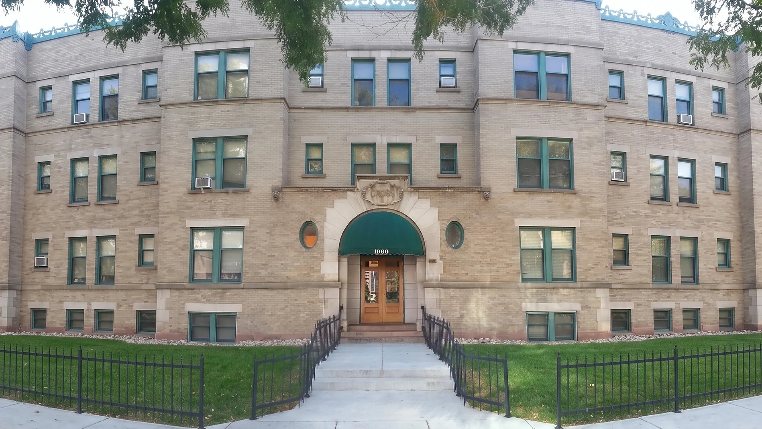 Charming vintage apartment building with a classic brick facade, lush green lawn, and welcoming entrance.