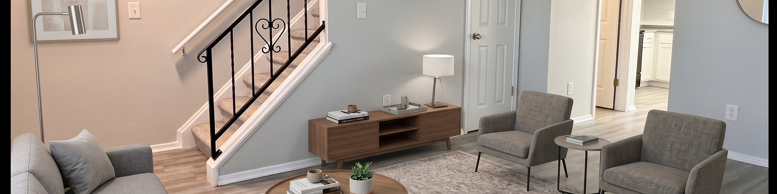 Inviting living room with modern gray sofa, elegant accent chairs, stylish coffee table, and stairs leading to upper level. Bright and airy space perfect for relaxation.