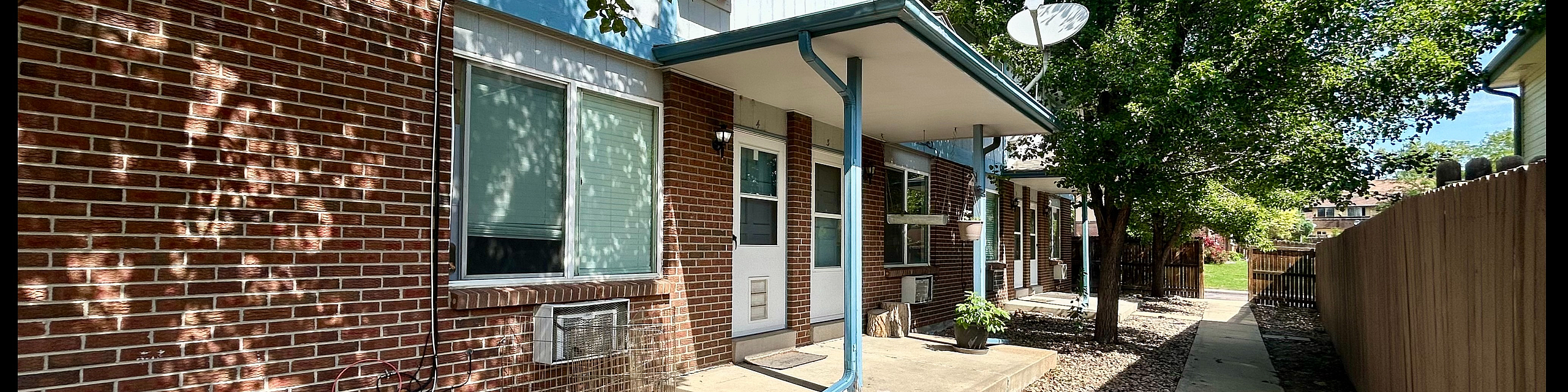 Charming brick apartment exterior with lush trees, a cozy walkway, and welcoming entrance.