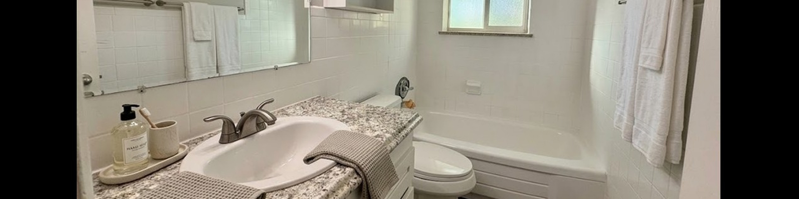 Bright and modern bathroom with elegant granite countertop, stylish lighting, and a pristine bathtub, offering a refreshing and serene atmosphere.