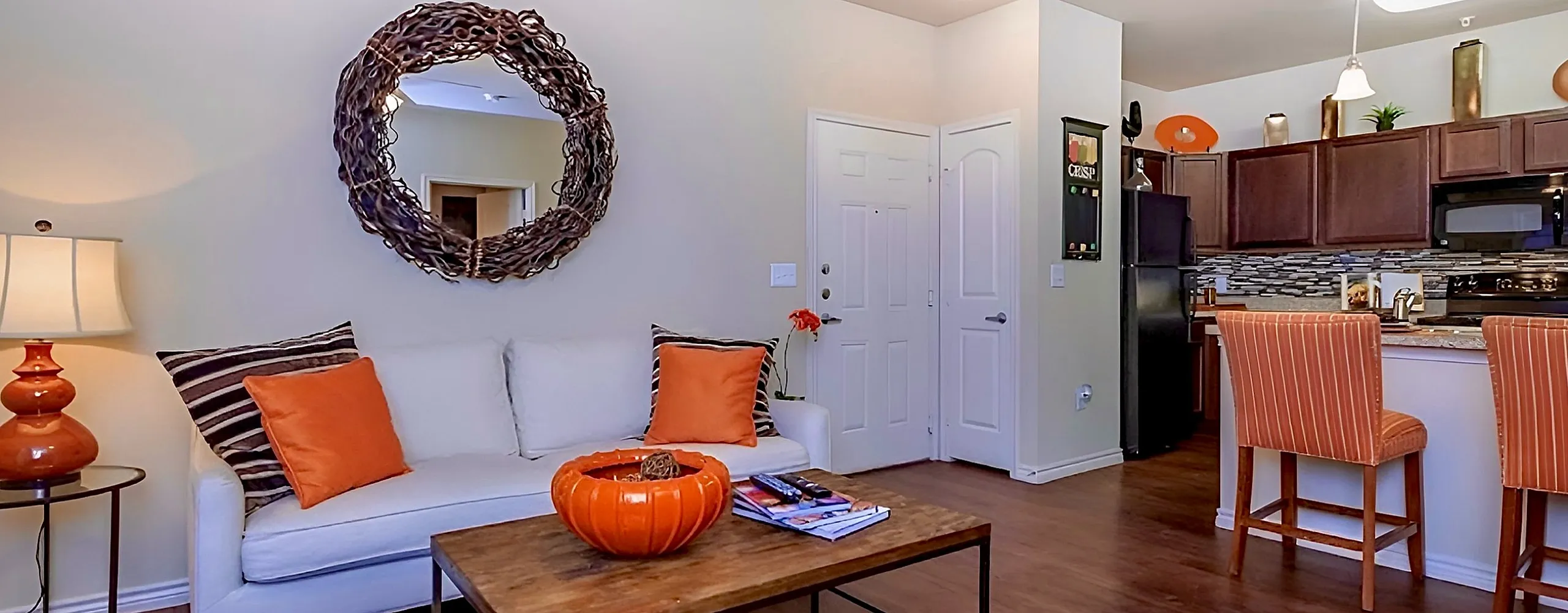 Inviting living space with cozy white sofa, vibrant orange accents, and an elegant open kitchen featuring sleek cabinets and modern appliances.