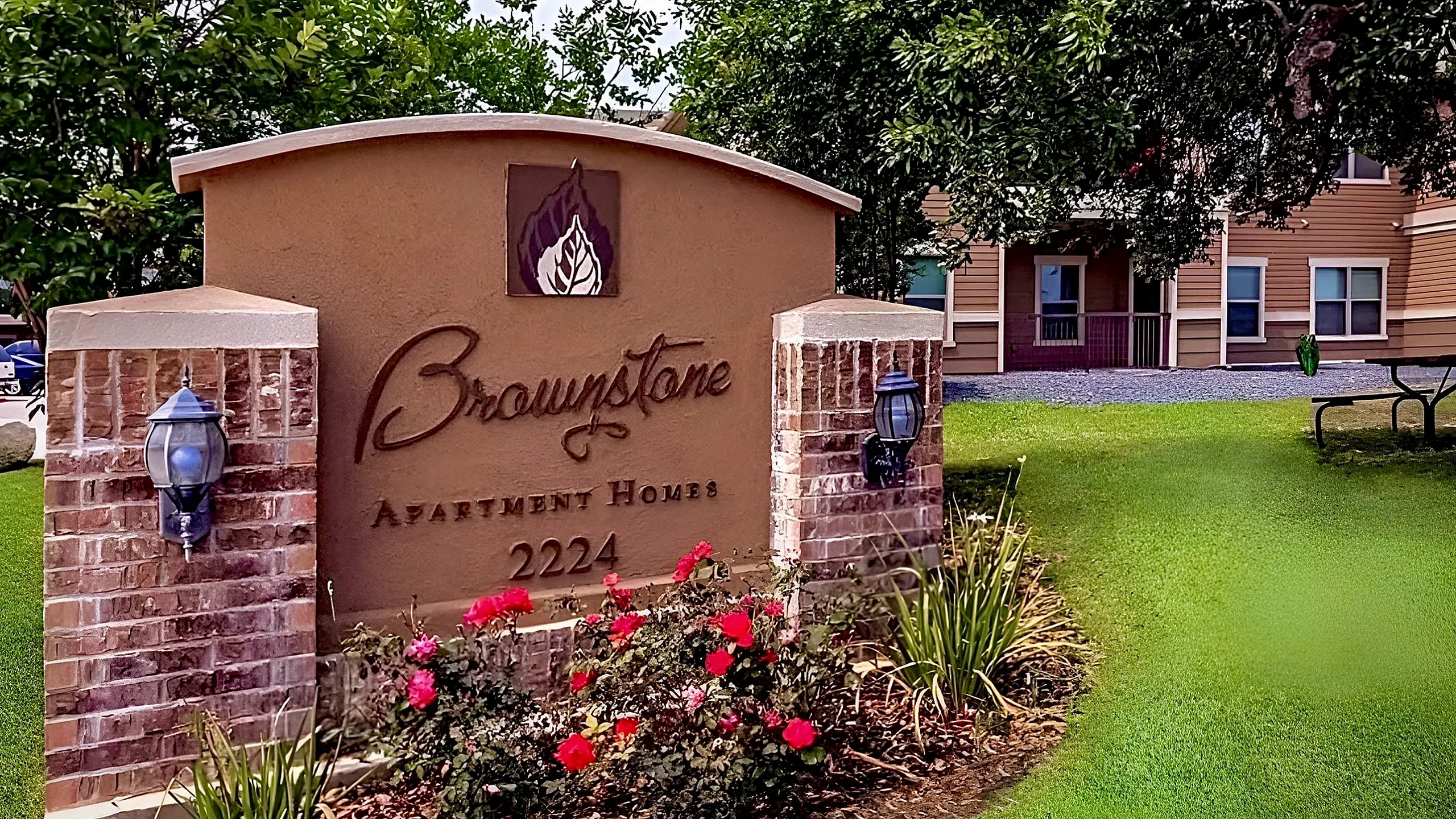 Brownstone Apartment Homes sign surrounded by vibrant flowers and lush greenery, leading to a picturesque residential entrance.