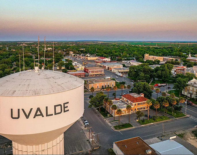 Scenic aerial view of Uvalde cityscape at dusk, showcasing lush greenery and charming architecture with a prominent water tower in the foreground.