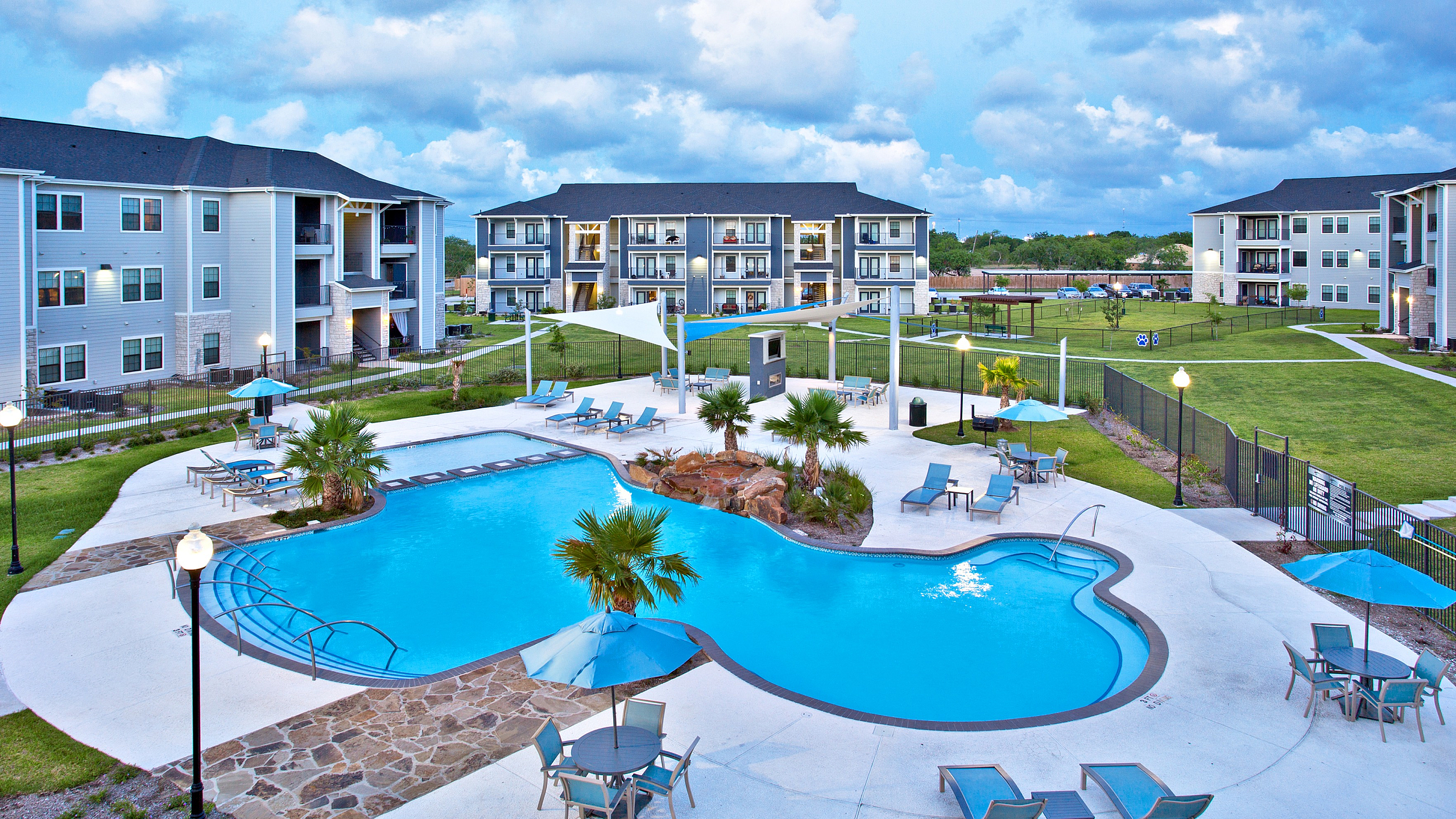 Elegant apartment complex with contemporary design, featuring a stunning resort-style pool surrounded by comfortable lounge chairs and lush landscaping.