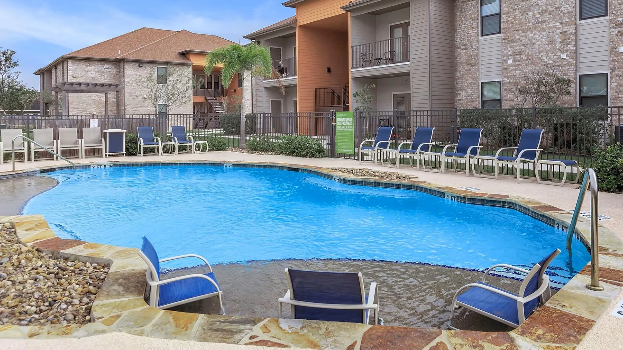 Inviting apartment complex boasting a sparkling outdoor pool, surrounded by comfortable lounge chairs and vibrant landscaping, perfect for relaxation and enjoyment.