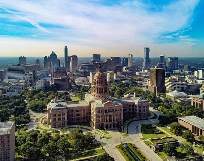 Breathtaking aerial view of a vibrant cityscape with a historic domed building surrounded by lush greenery, against a backdrop of modern high-rises and a clear blue sky.