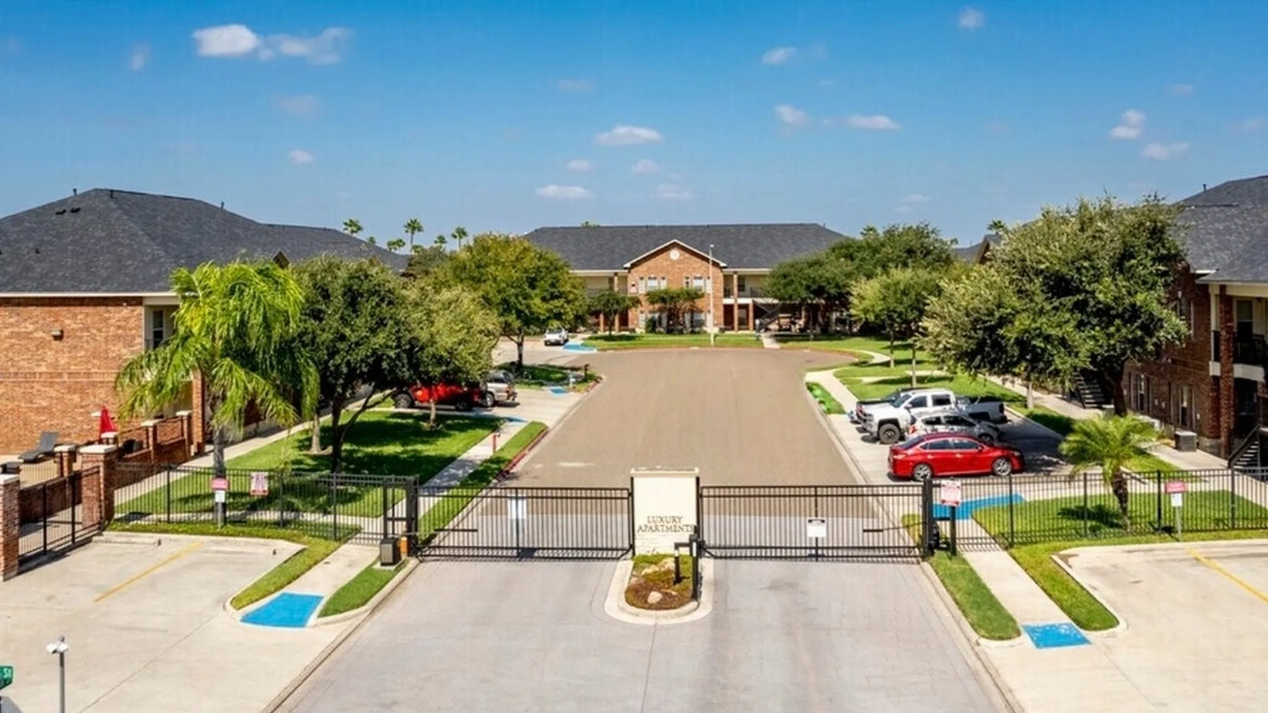 Inviting gated community with brick buildings, lush greenery, and vibrant landscaping under a clear blue sky.
