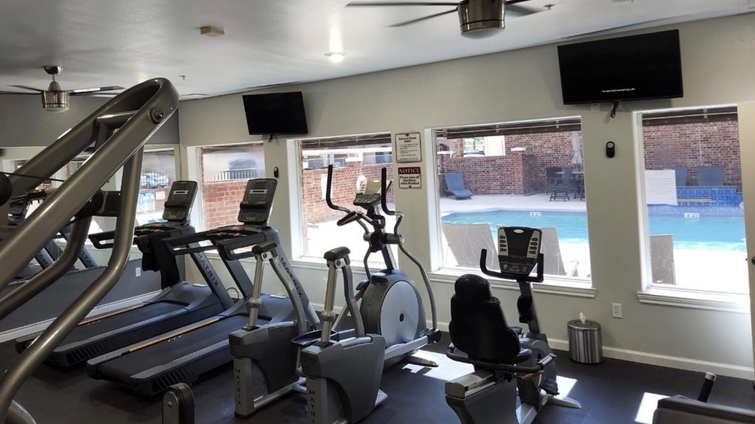 Modern apartment gym with state-of-the-art treadmills and elliptical machines, offering a pool view for an invigorating workout experience.