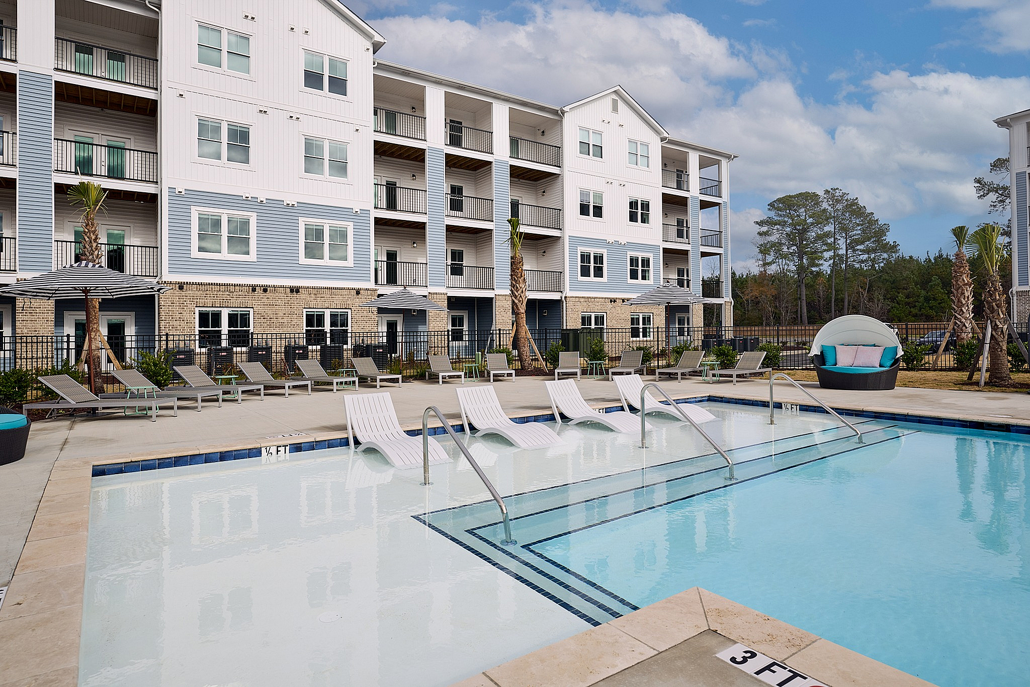 Elegant apartment complex with poolside lounge chairs and modern design.