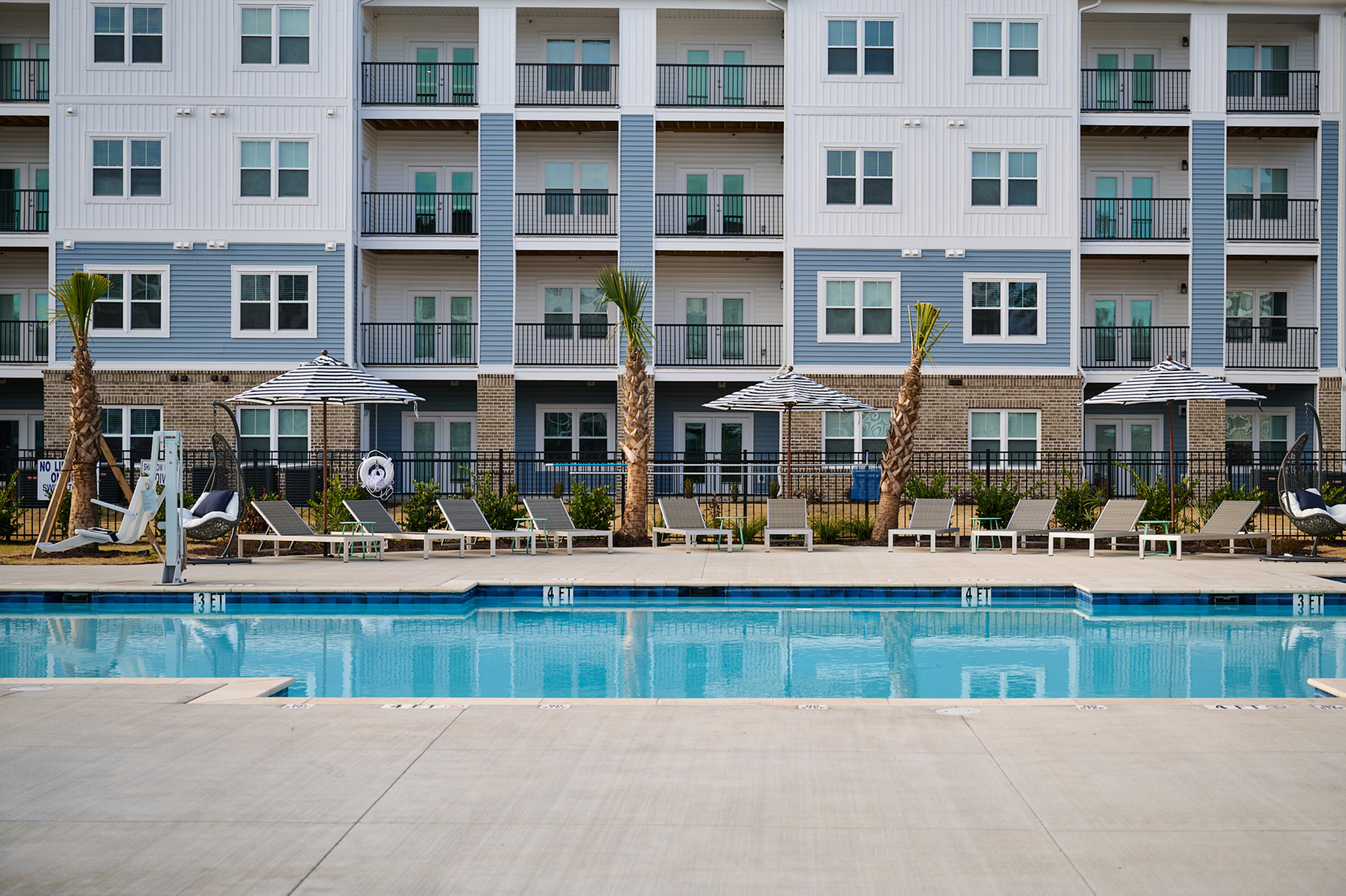 Chic apartment building facade with a pristine pool and comfortable sun loungers.