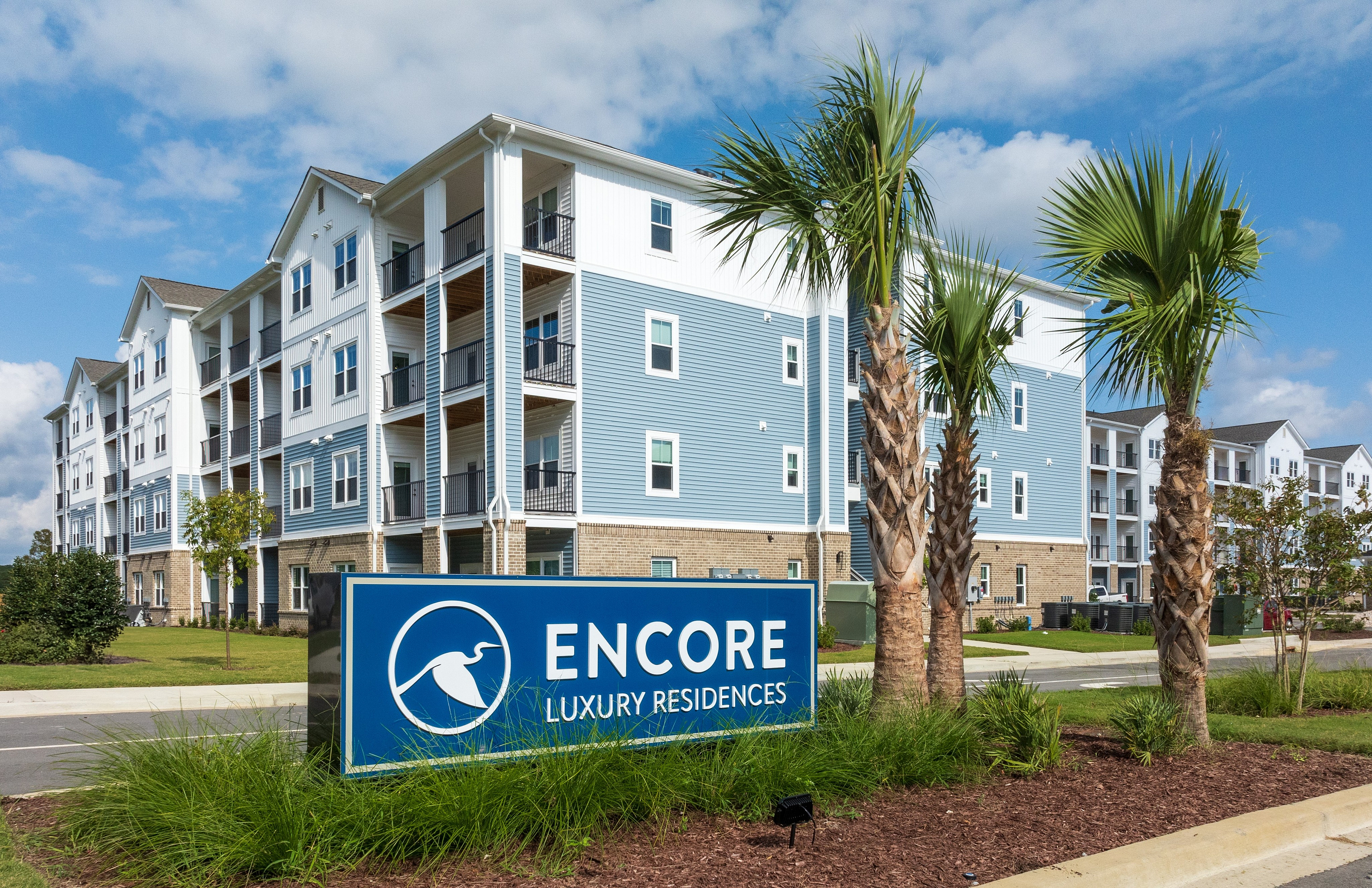 Stunning modern apartment building with elegant blue and white exterior, surrounded by lush landscaping.
