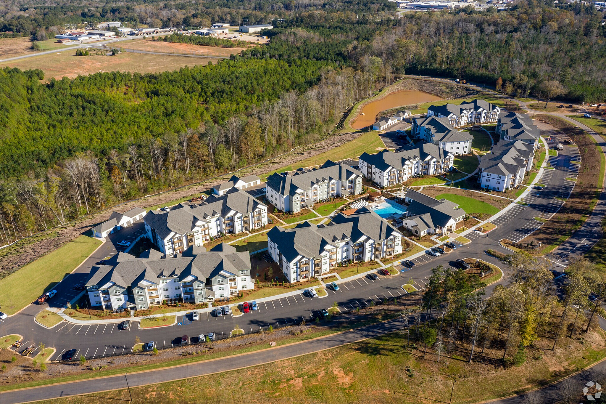 Aerial view of a modern apartment complex with lush surroundings, a central pool, and ample parking.