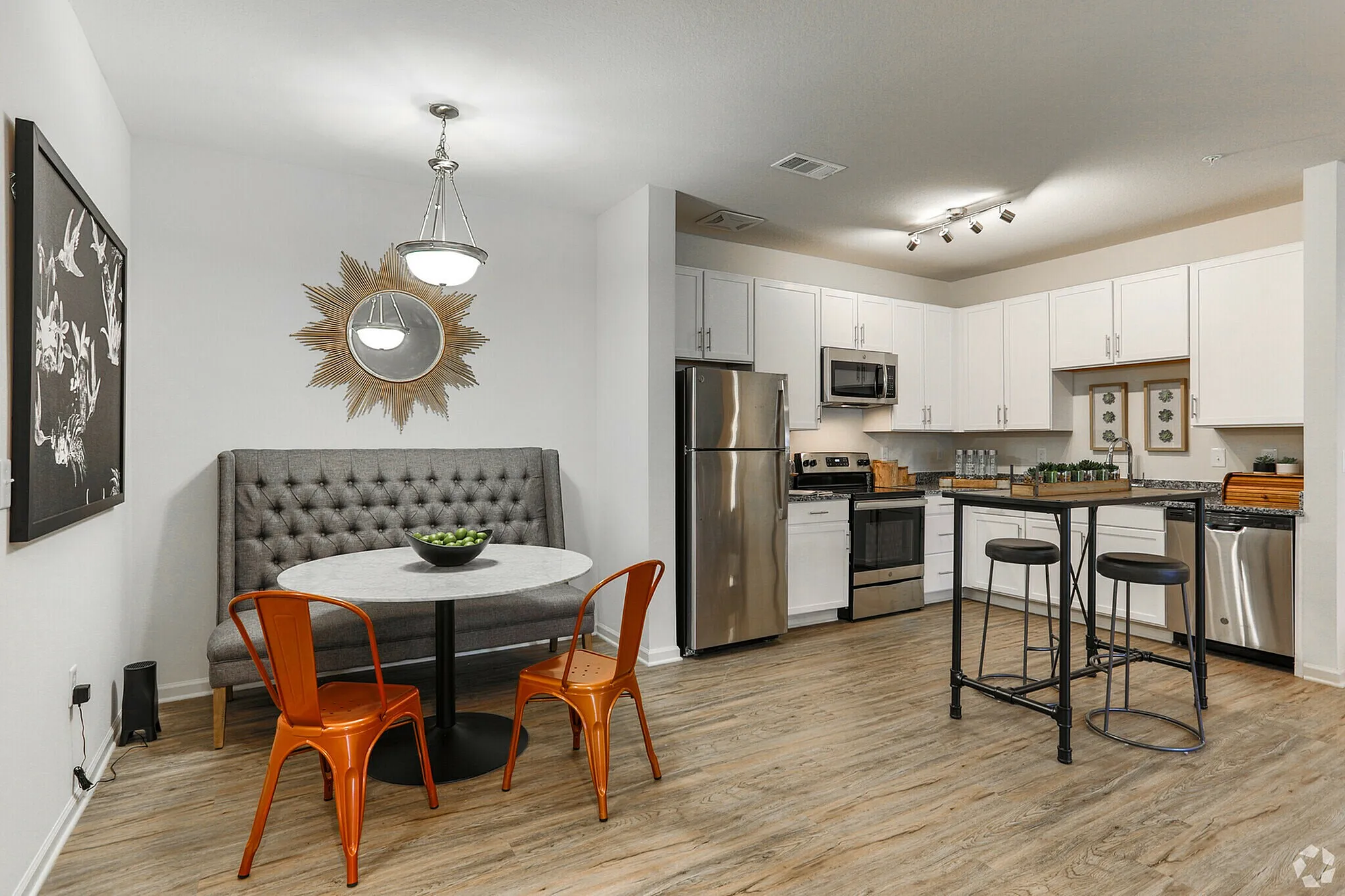 Stylish kitchen with white cabinets, stainless steel appliances, and a cozy dining nook with orange chairs.