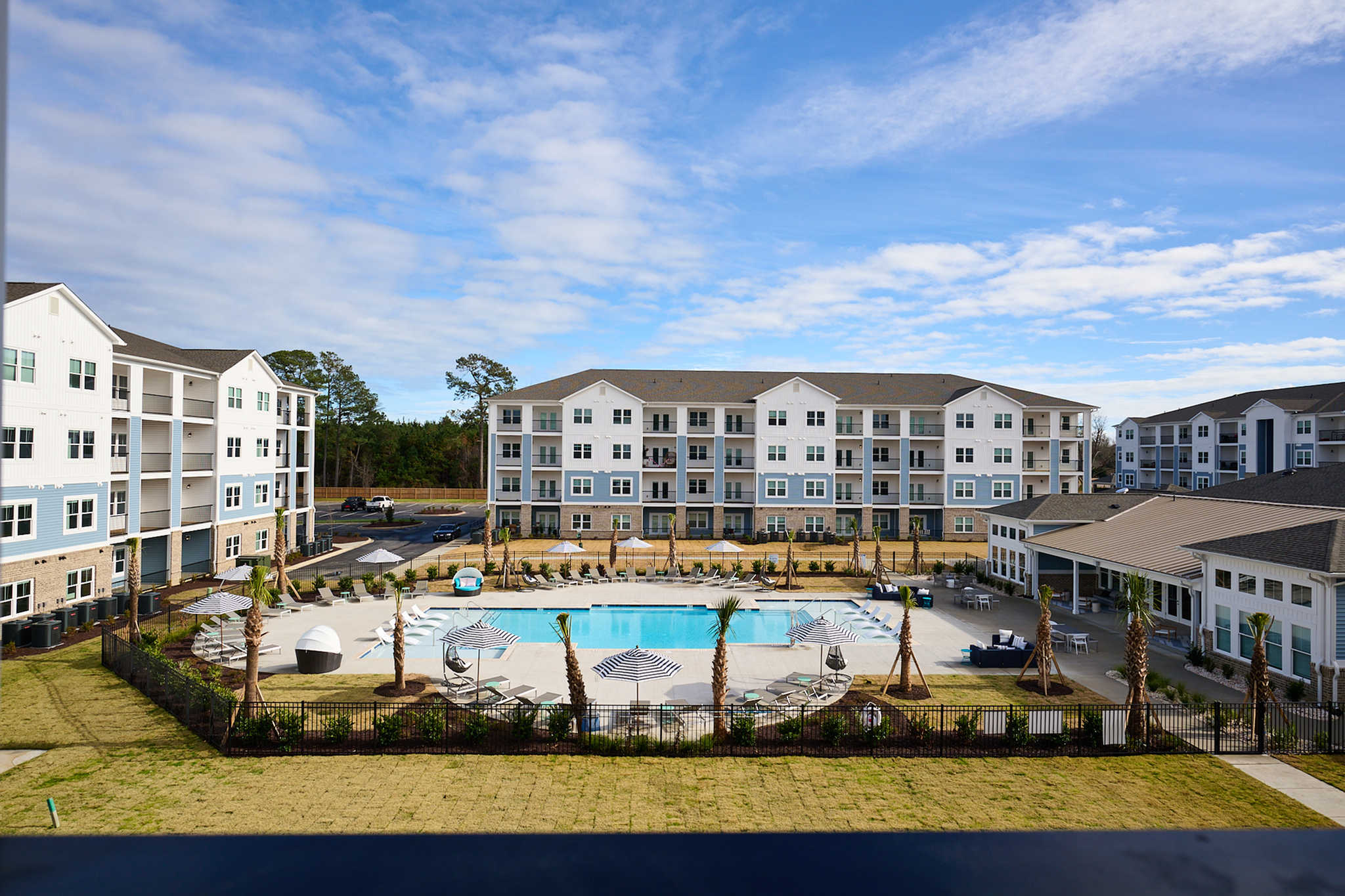 Aerial view of a modern apartment complex with a pristine pool area surrounded by lush landscaping.