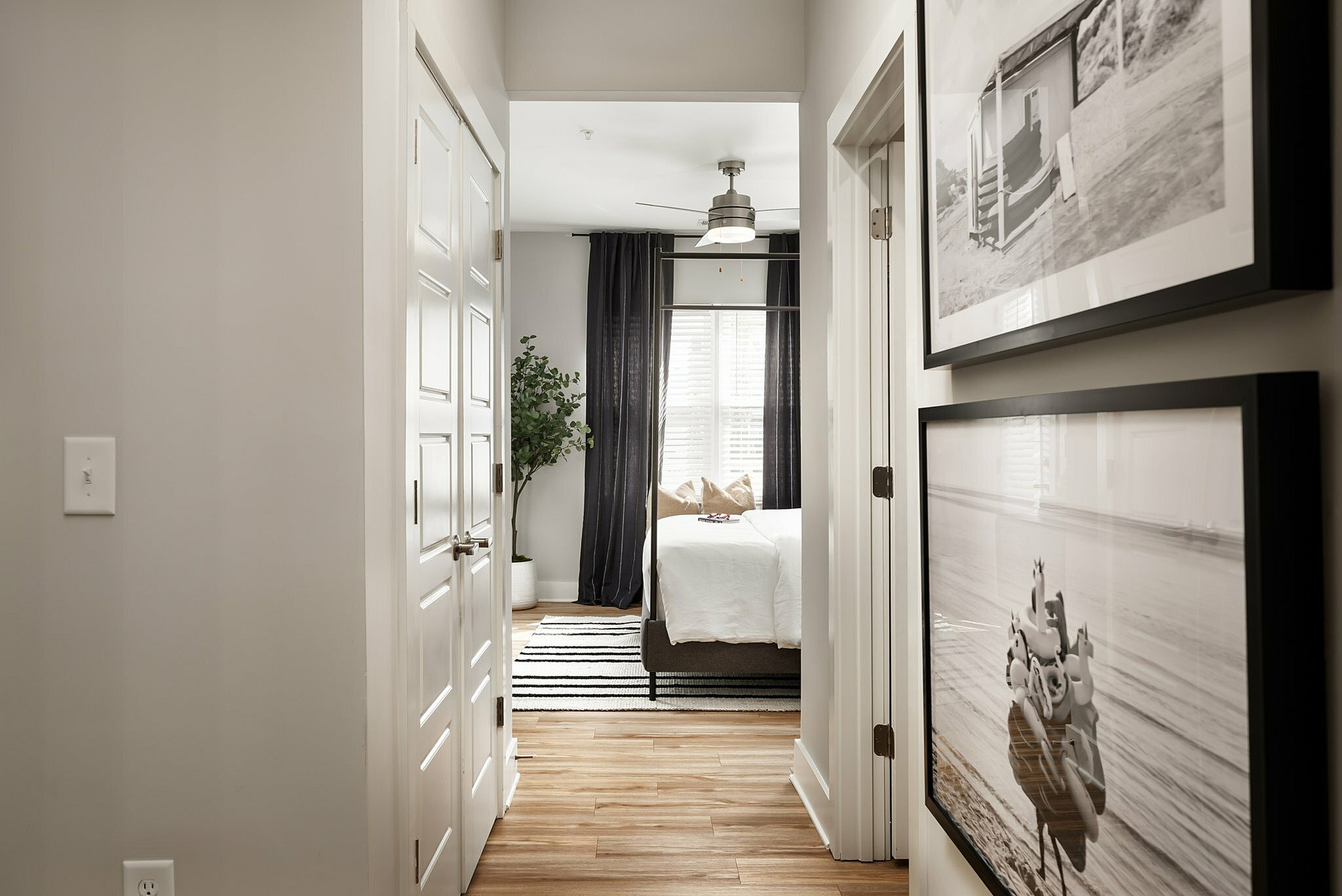 Corridor view leading to a bright bedroom with elegant decor, featuring framed wall art and wooden flooring.