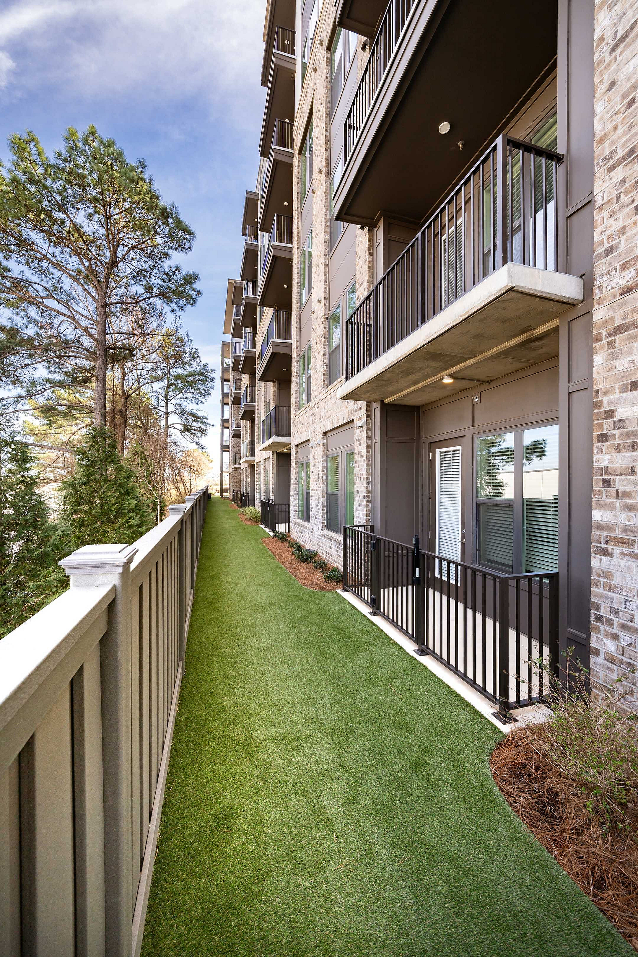 Modern apartment building with private balconies, lush green landscaping, and a serene tree-lined walkway.