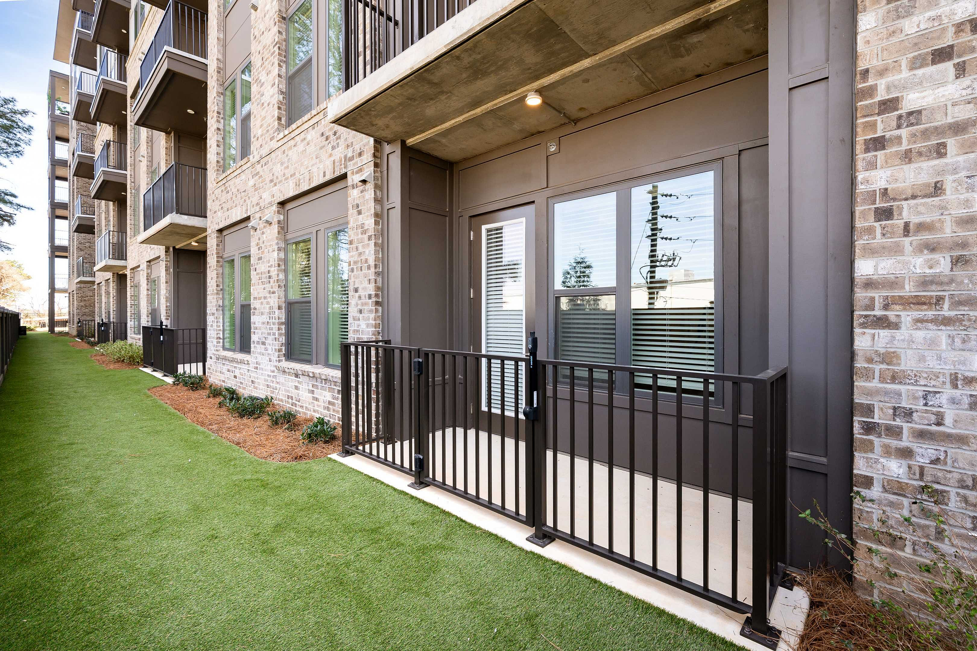 Modern apartment building with elegant brick facade and private balconies overlooking a lush green lawn.