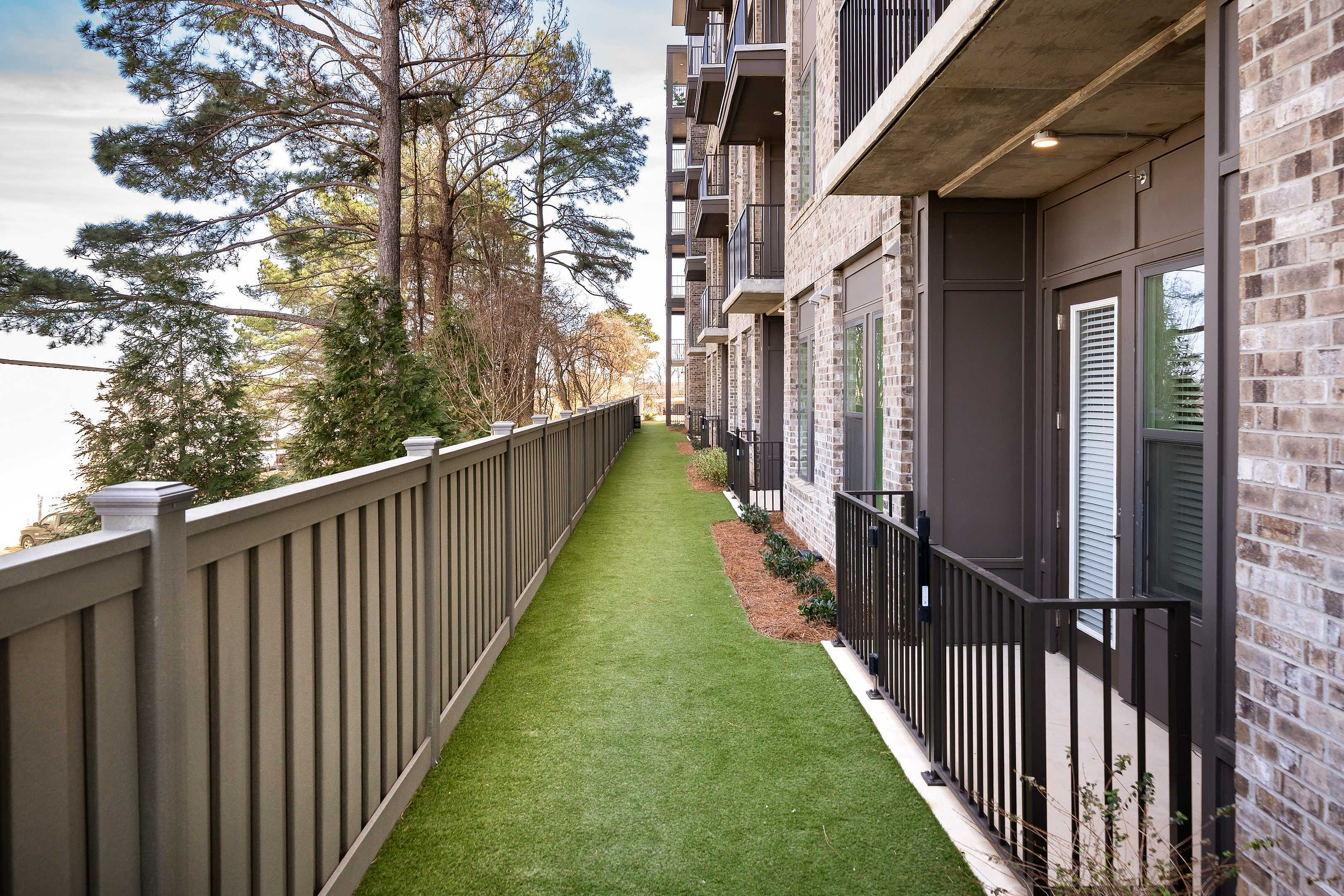 Charming apartment exterior featuring lush green pathway, modern brick design, and private balconies, surrounded by serene trees.