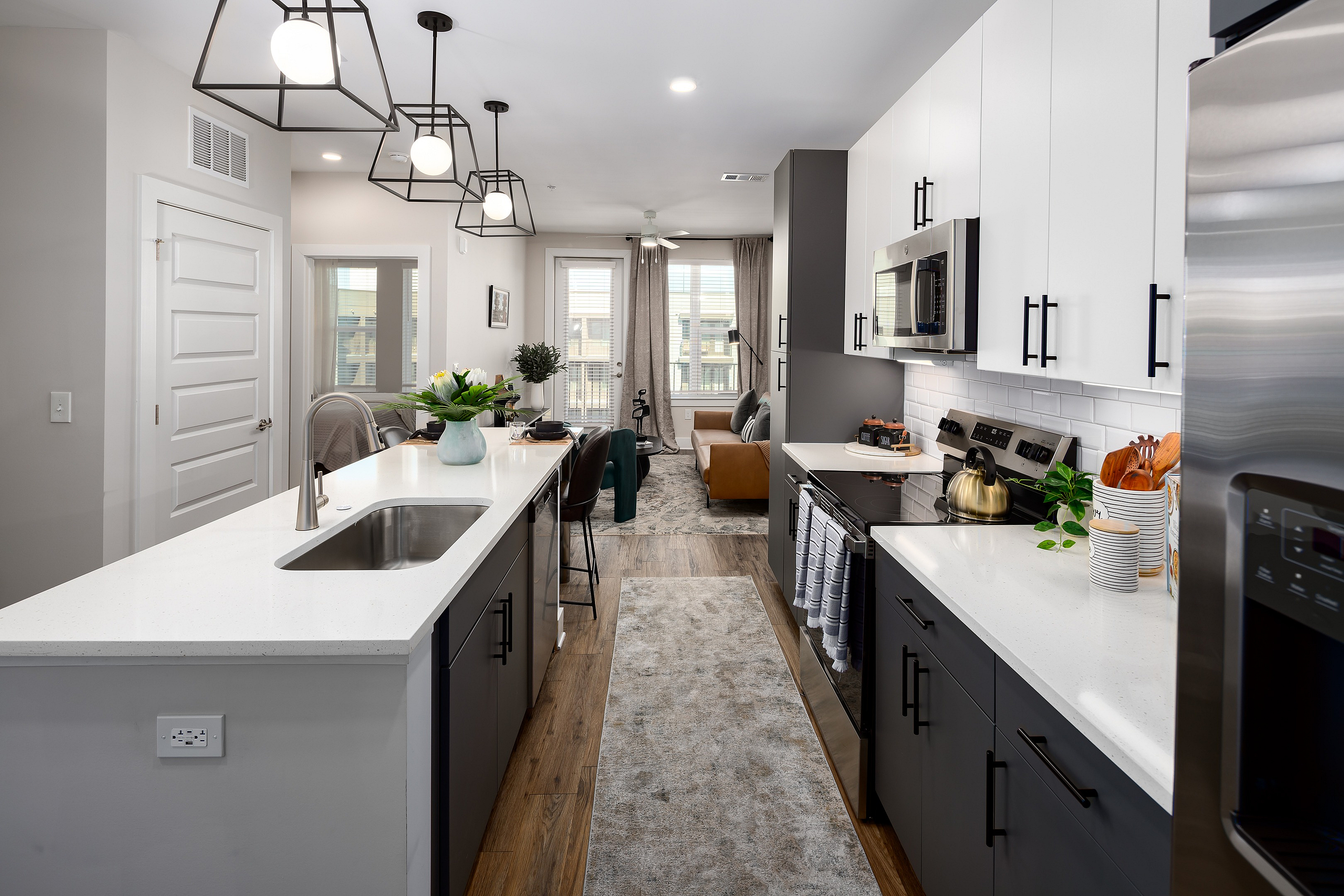 Modern apartment kitchen with sleek countertops, elegant lighting, and cozy living area in the background.
