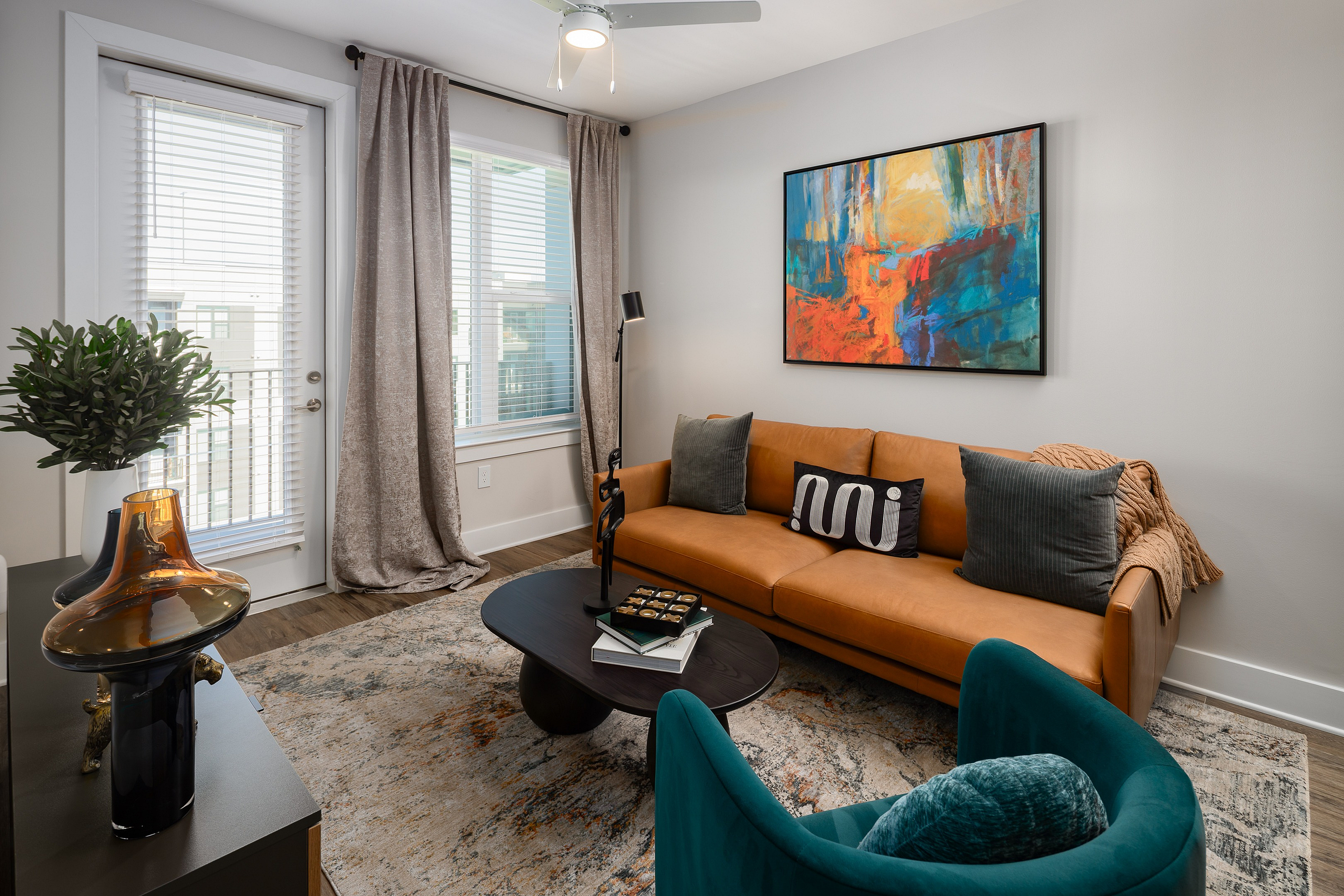 Contemporary living room with a stylish tan sofa, vibrant abstract wall art, and elegant decor accents under natural light from large windows.