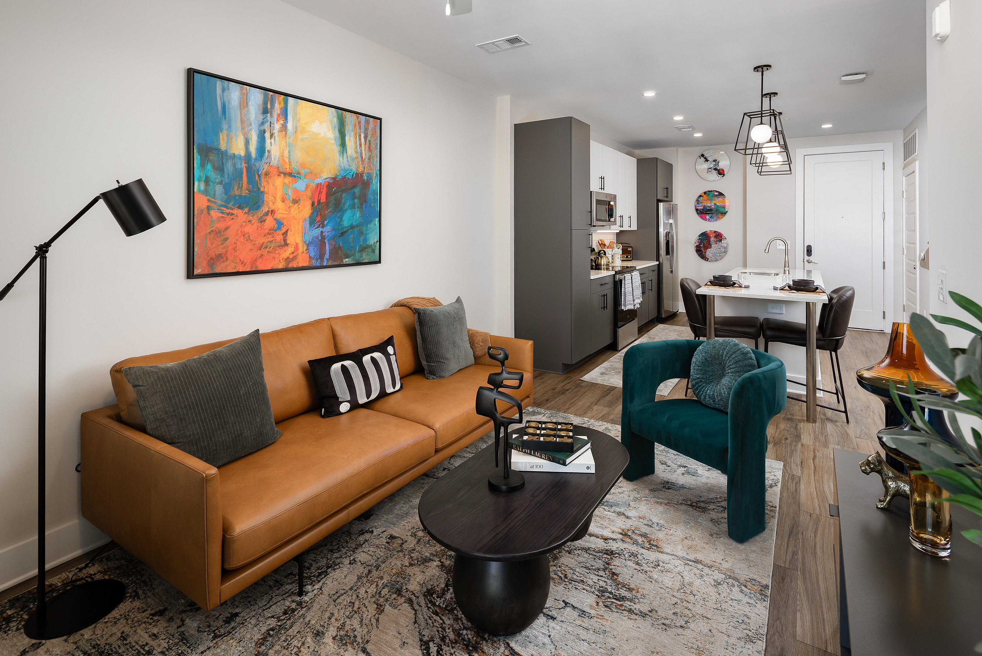 Modern open-concept living area showcasing a cozy brown leather sofa, vibrant artwork, and a sleek kitchen with stainless steel appliances.